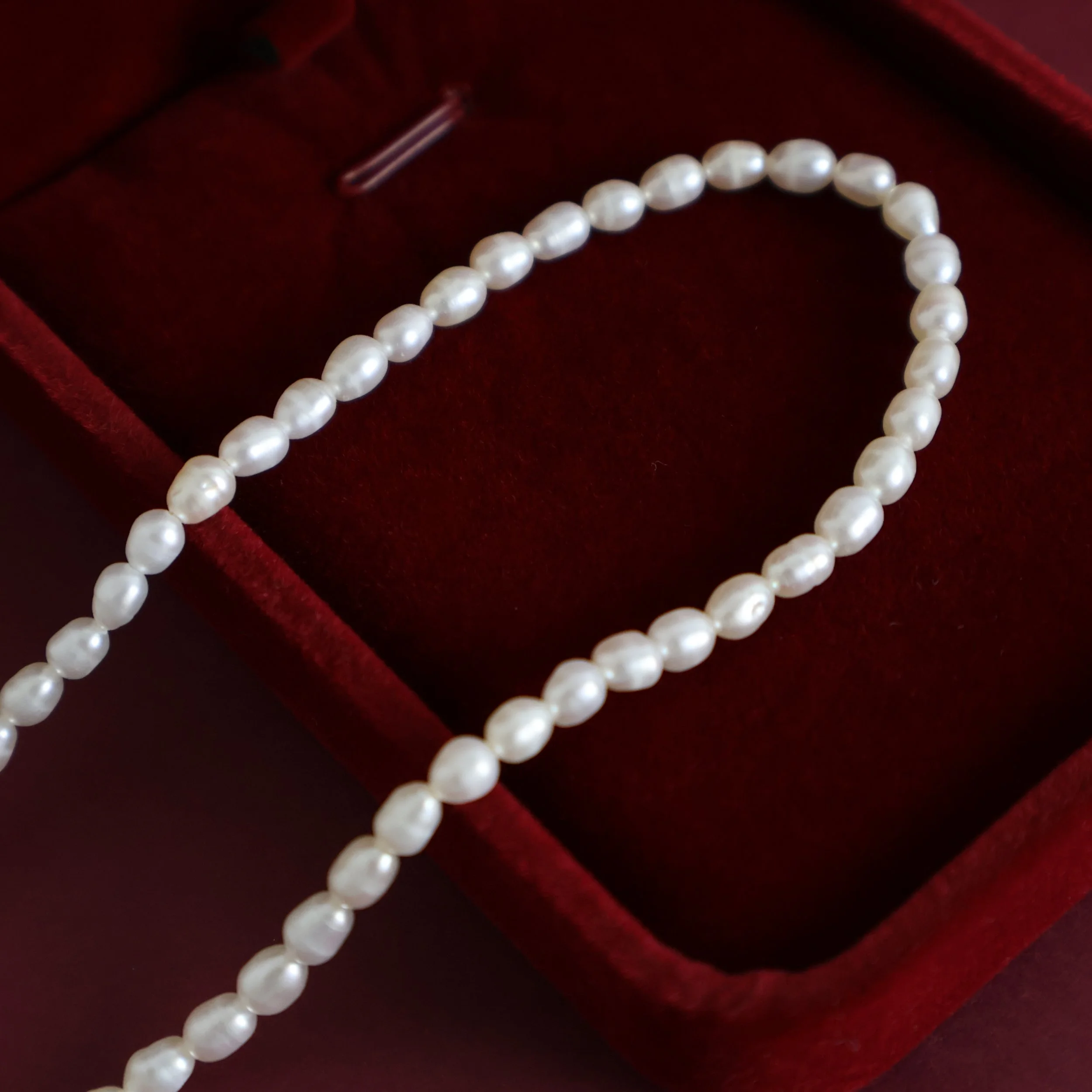 Macro photograph of natural white freshwater rice pearls with irregular oval shapes and soft lustre on a burgundy velvet jewellery box.