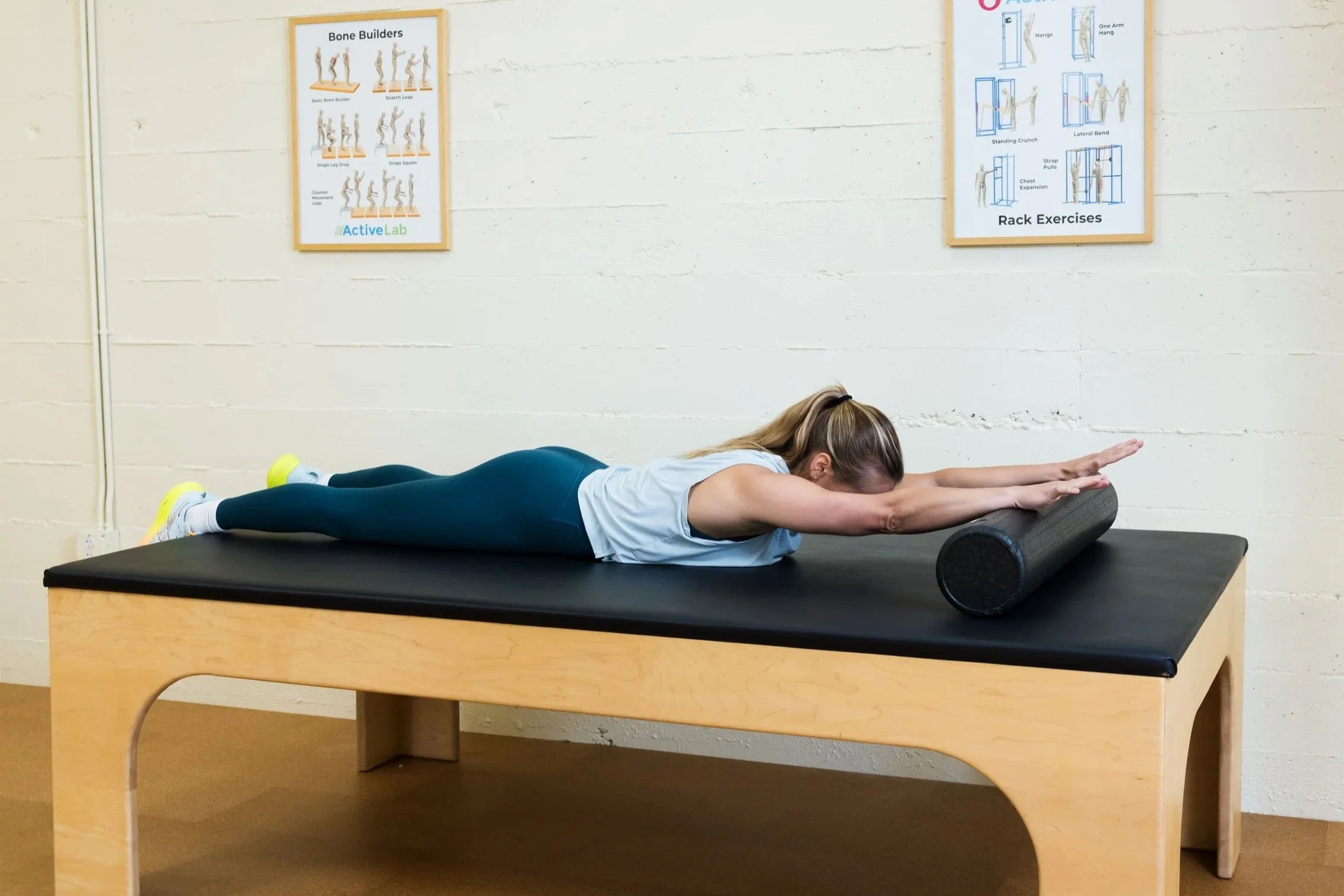 Photo of a woman in athletic attire, lying belly-down on a padded exercise table at ActiveLab gym in Vancouver, WA, using a foam roller under her hands and wrists to roll out and stretch her spine