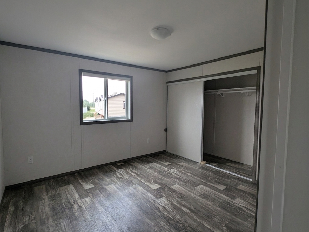 An empty room with beige walls, gray trim, a window showing the outside, and an open closet with a sliding door.
