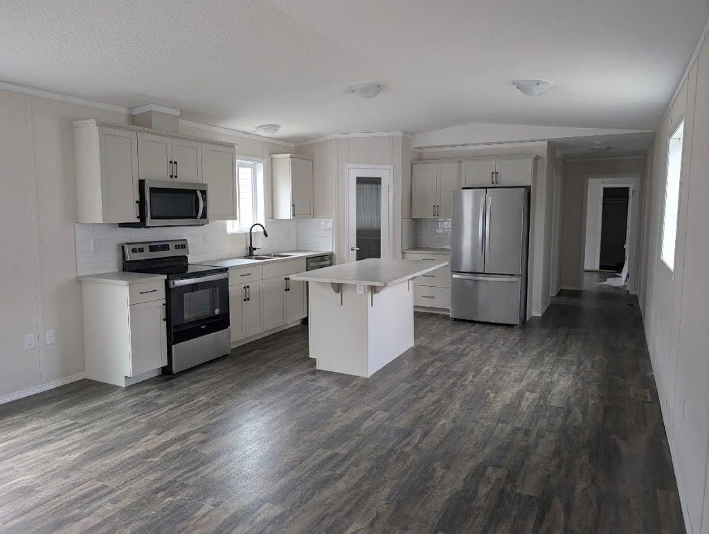 A modern kitchen with white cabinets, stainless steel appliances, a small island, and wood-like flooring.