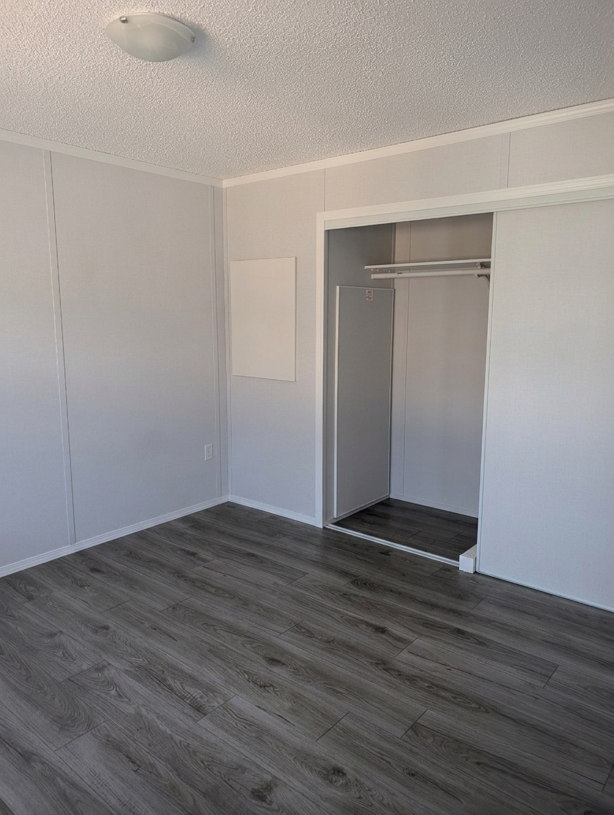 Empty room with white walls, gray wood floor, and open closet with sliding door.