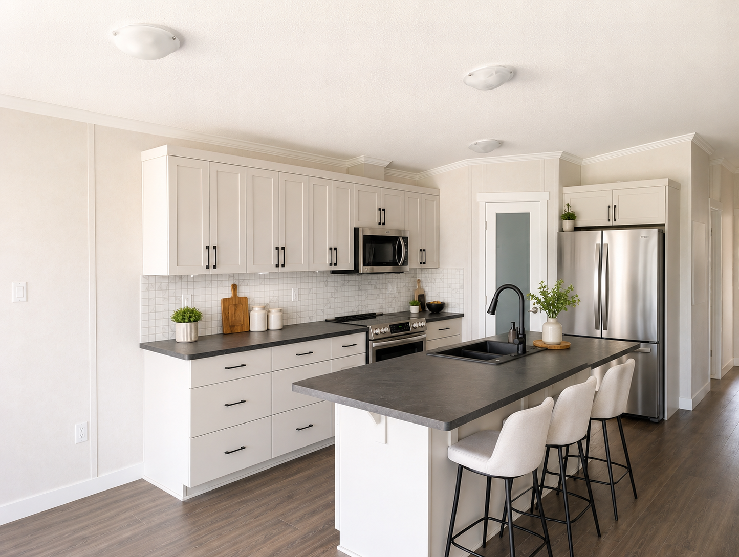 Modern kitchen with white cabinets, black countertops, stainless steel appliances, and a kitchen island with three beige barstools.