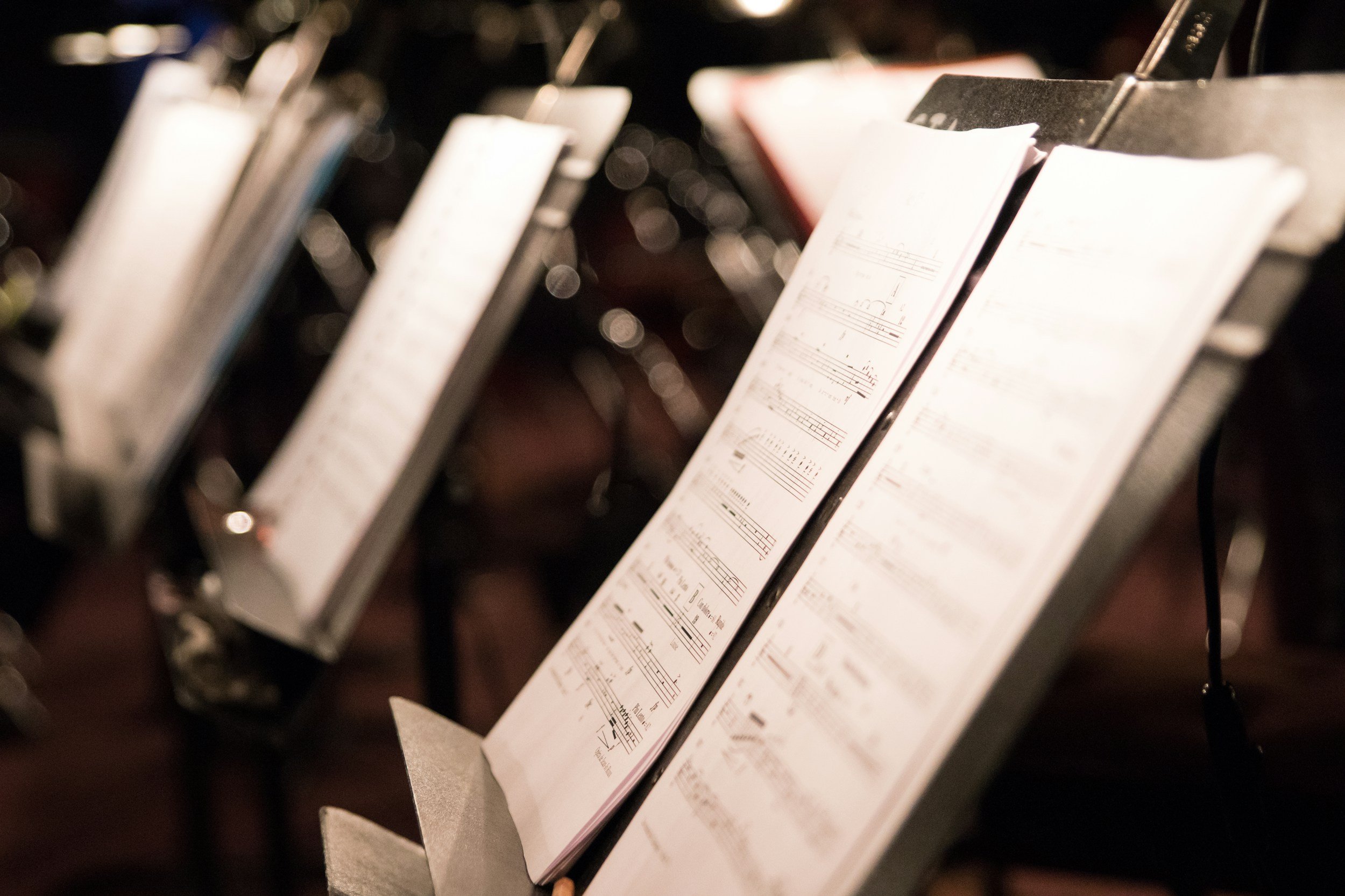Close-up of sheet music on music stands in a dimly lit setting.