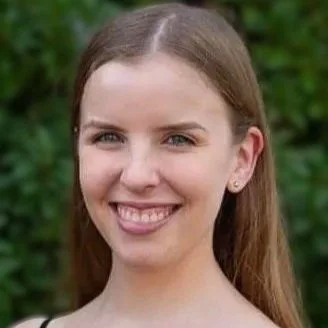A young woman with long brown hair smiling outdoors.