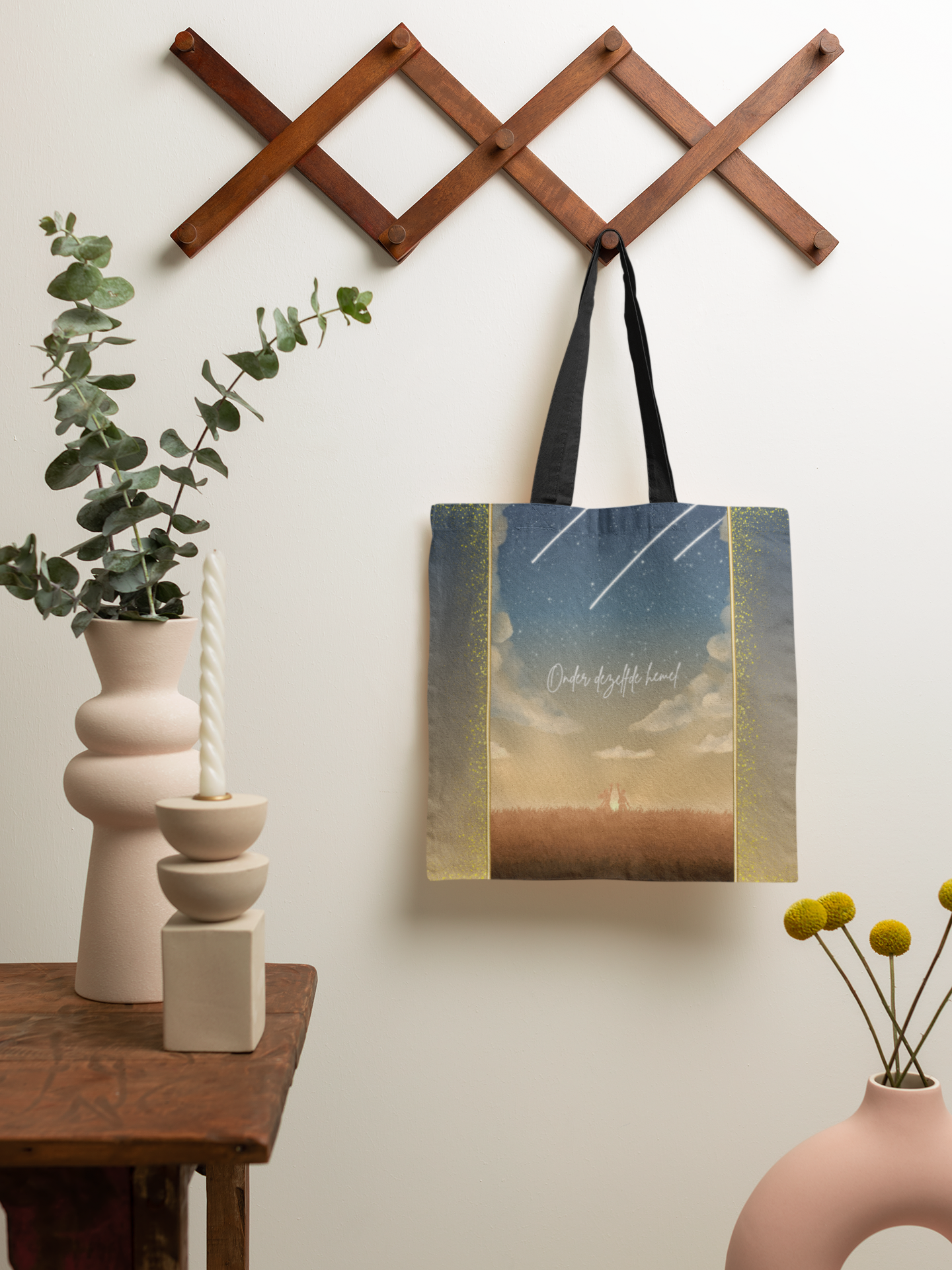 Celestial tote bag featuring shooting stars and silhouettes,  unique gift for expats living in the Netherlands. Bag is hanging on a coat rack with vases and candles sitting in front.