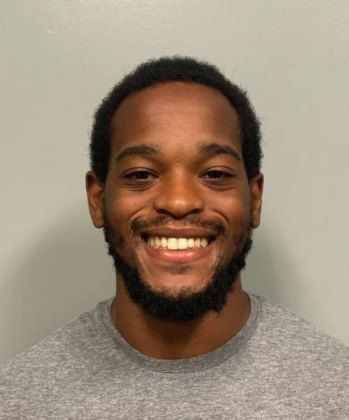 A smiling person wearing a gray shirt against a light colored background.