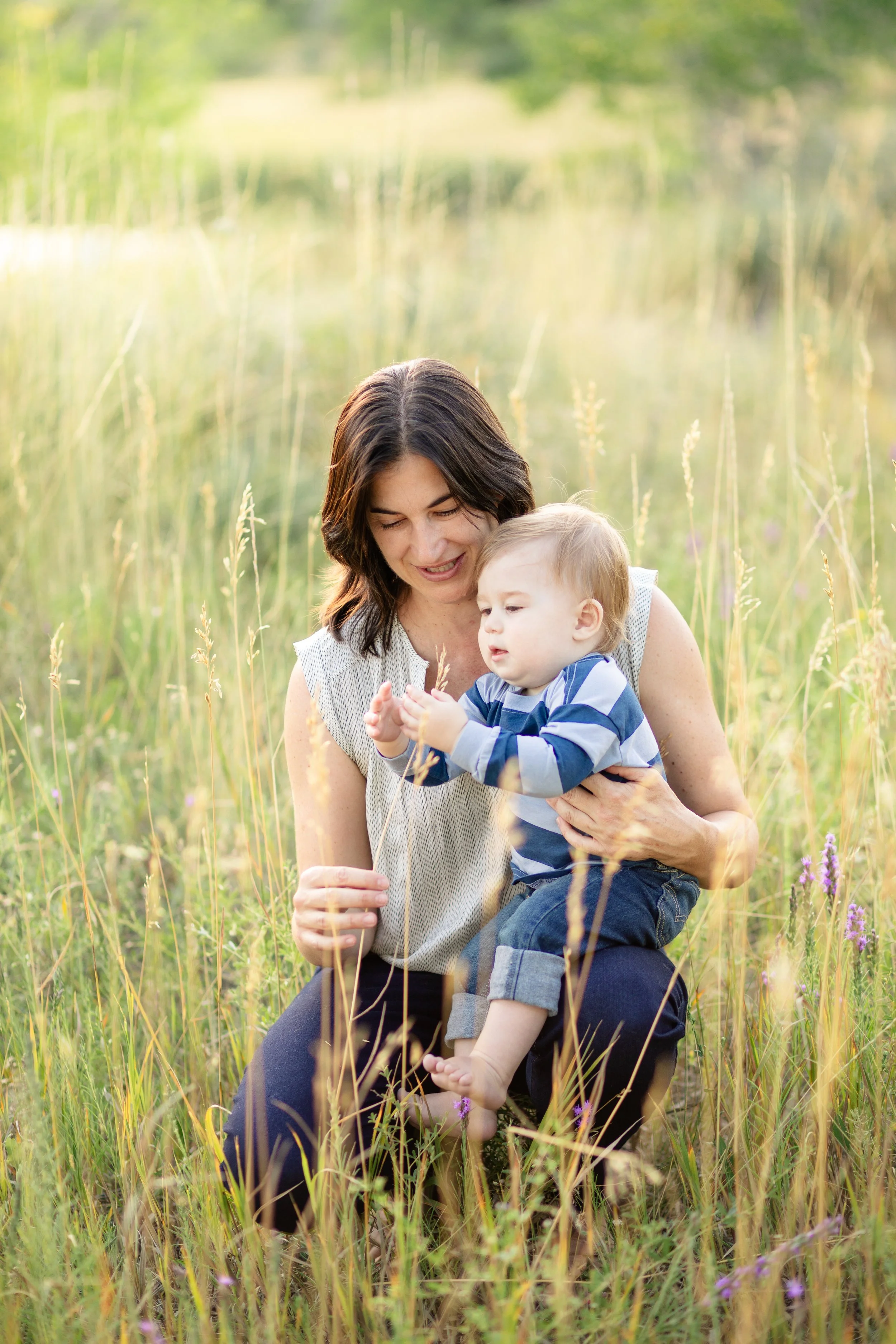 A woman and a toddler boy sitting in a grassy field surrounded by tall grasses and wildflowers in Boulder, CO
