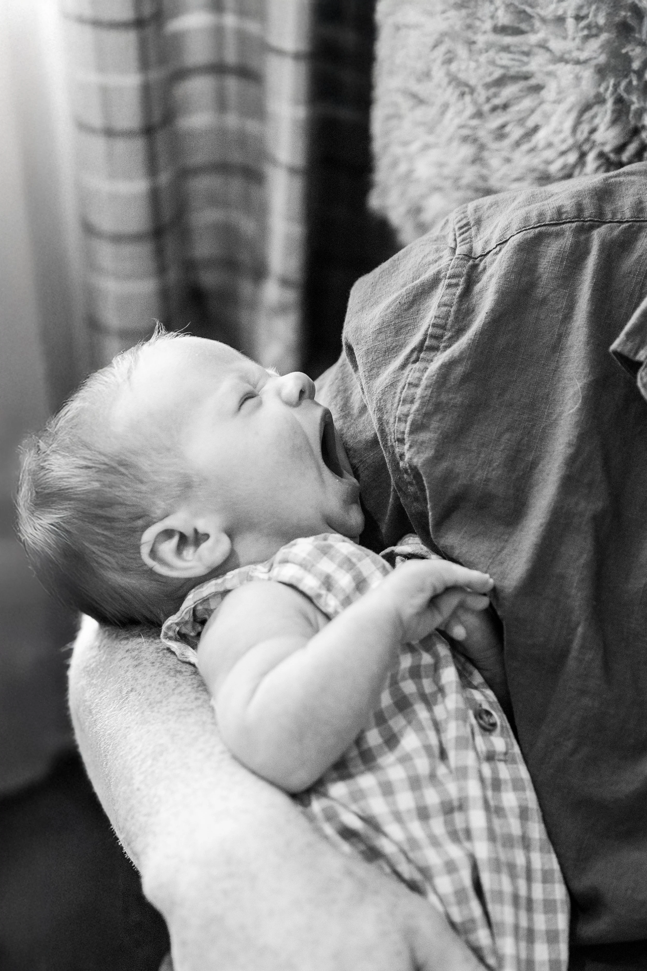 Father holds sleepy newborn son during an in-home newborn photography session near Fort Collins, Colorado.