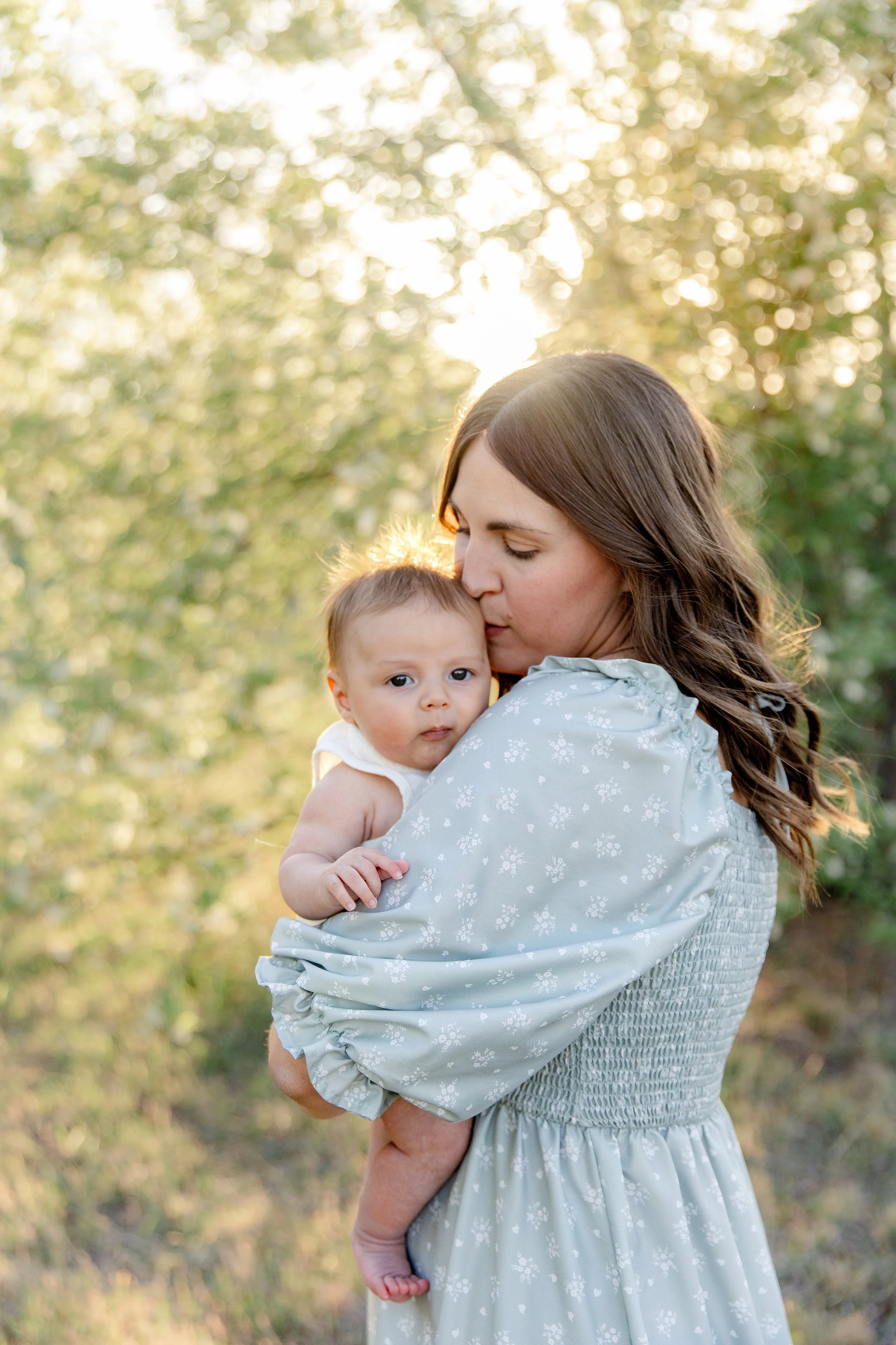 Mom kissing baby boy in front of tree during a Fort Collins family photography session.
