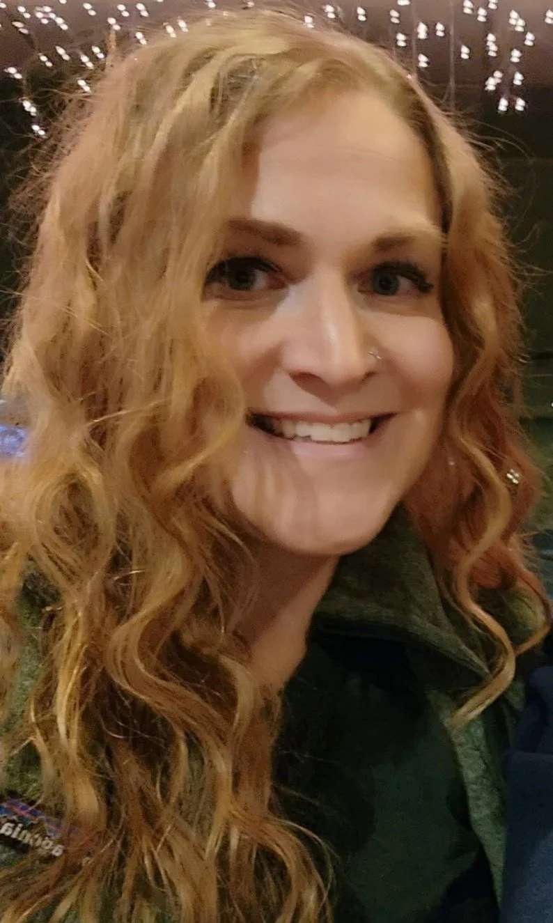 A woman with long, curly red hair smiling at the camera.
