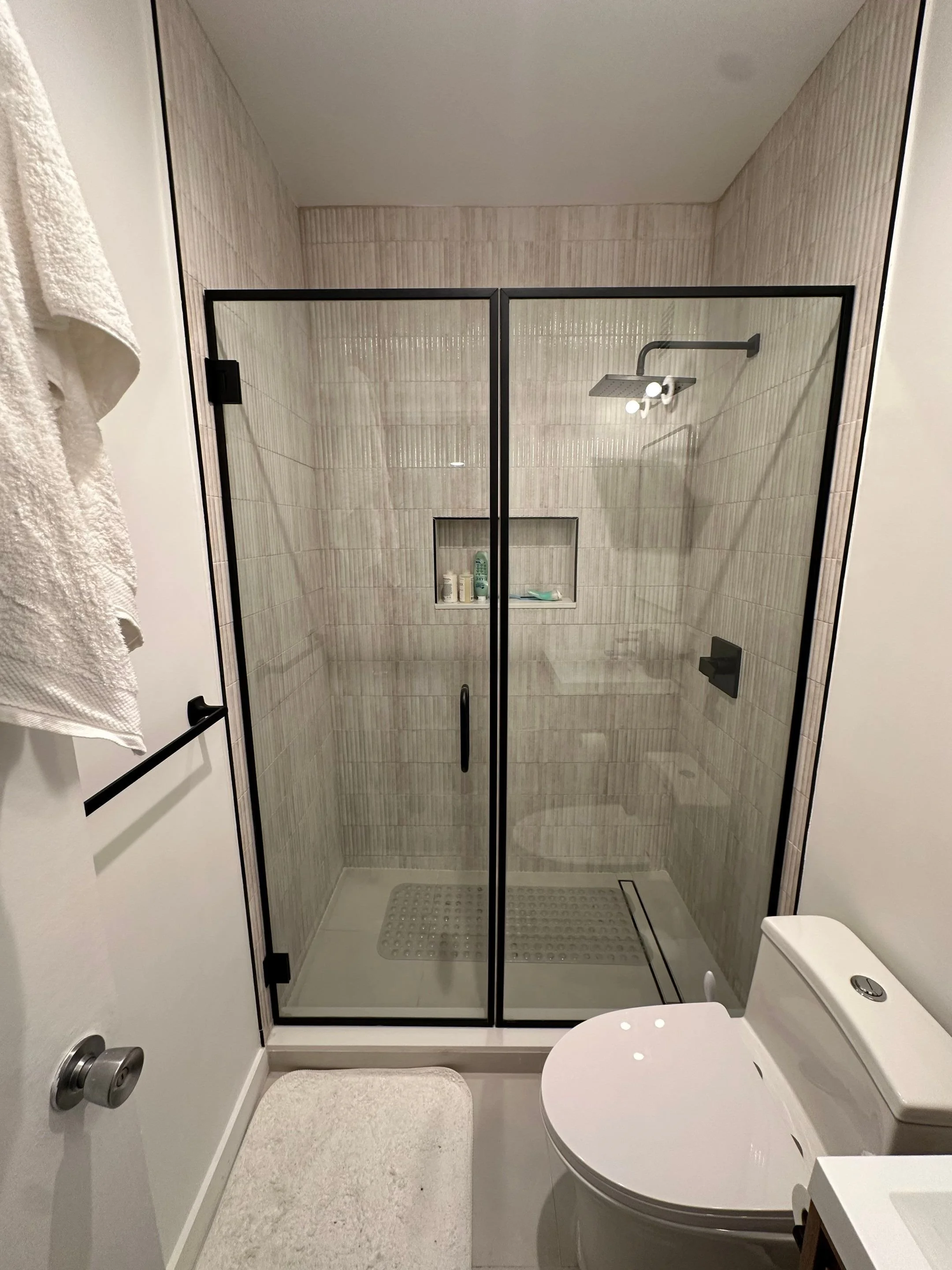 Bathroom with a glass shower enclosure, a toilet, a towel hanging on a bar, and a bath mat.