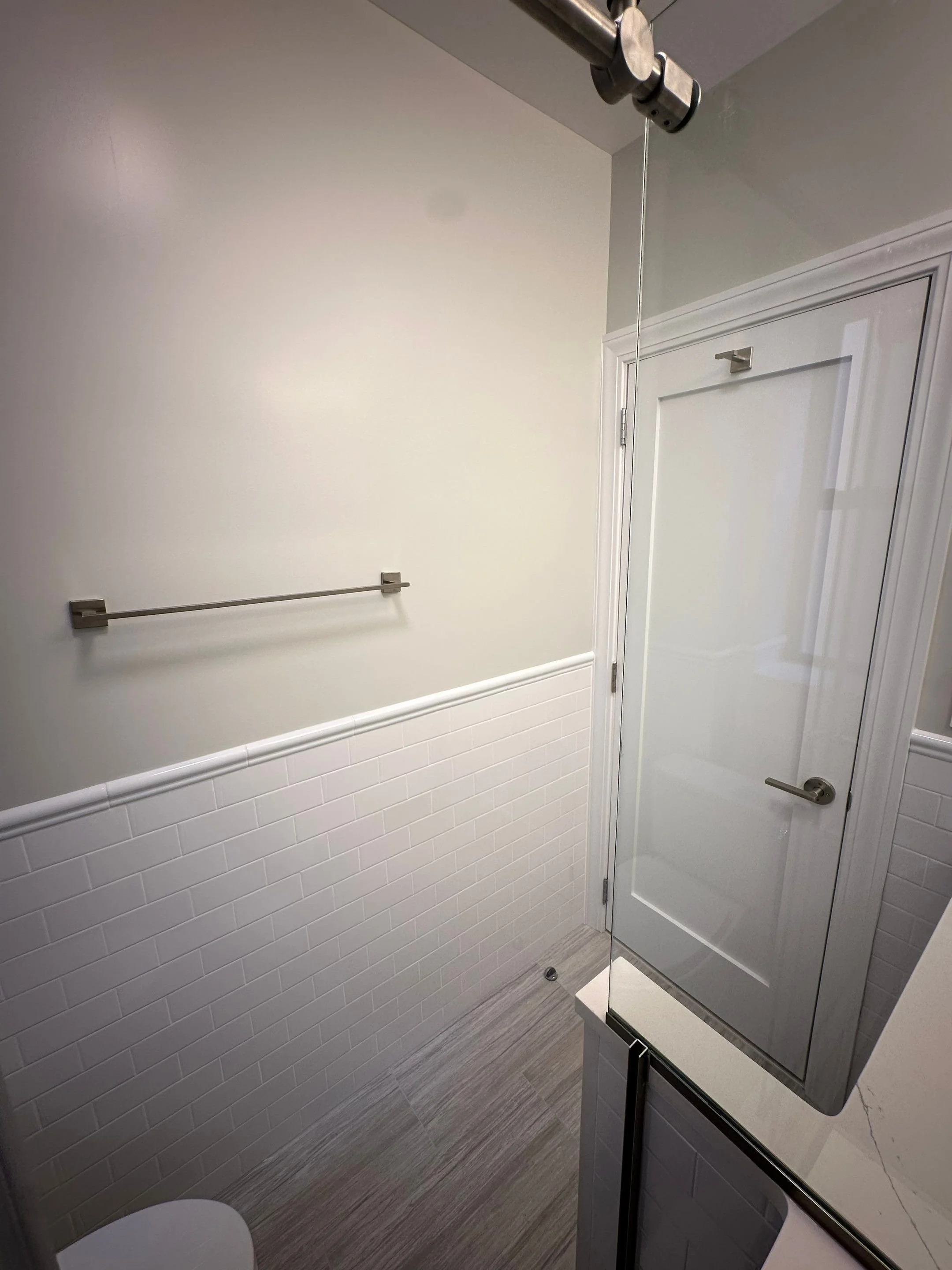 Small bathroom with white tiled lower half of the wall and plain upper wall, a towel bar, a closed door with a mirror, and a glass shower door.