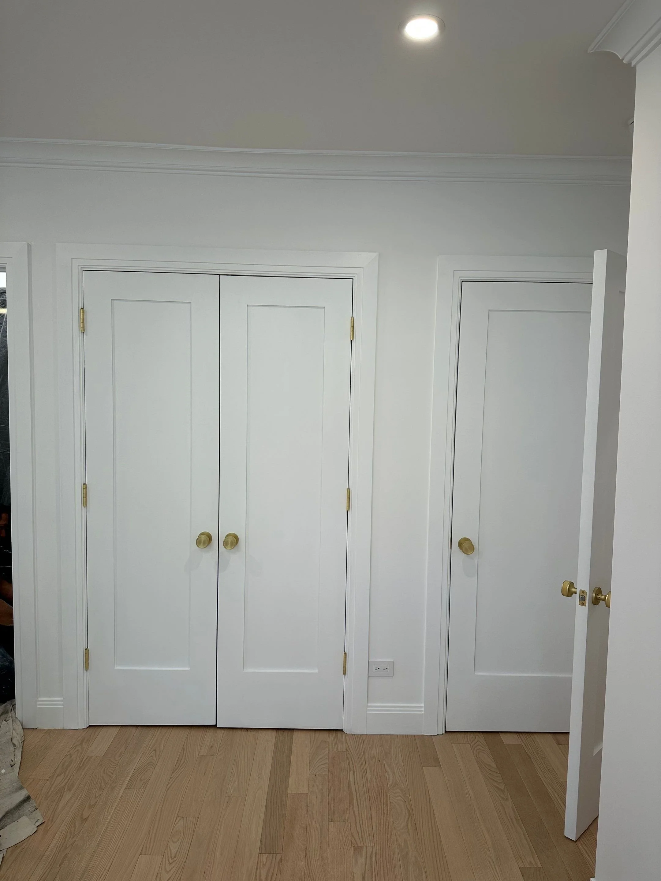 White closet doors with gold doorknobs, wooden floor, white walls, and ceiling with recessed lighting.