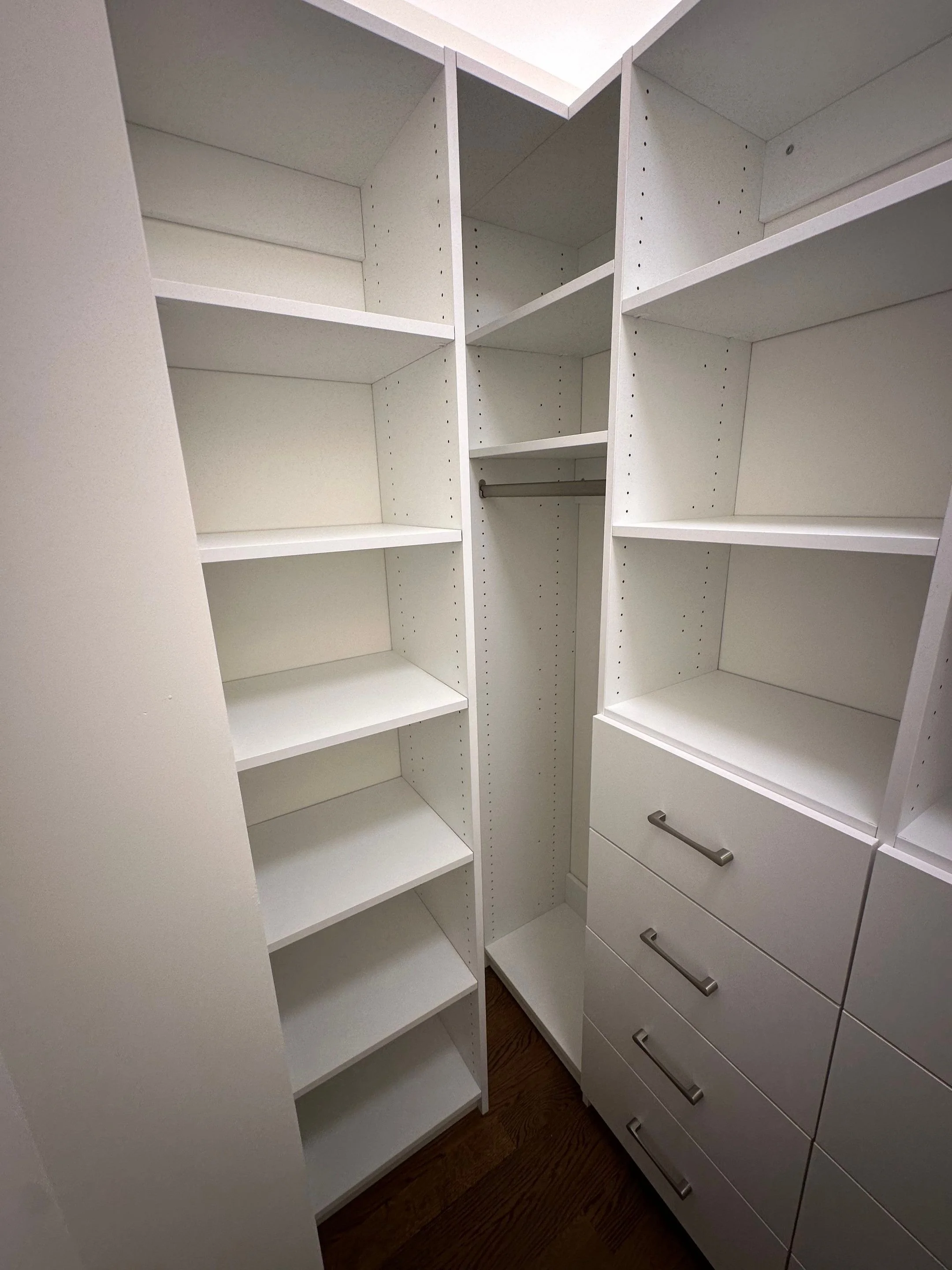 Empty white closet with shelves, drawers, and a metal rod for hanging clothes.