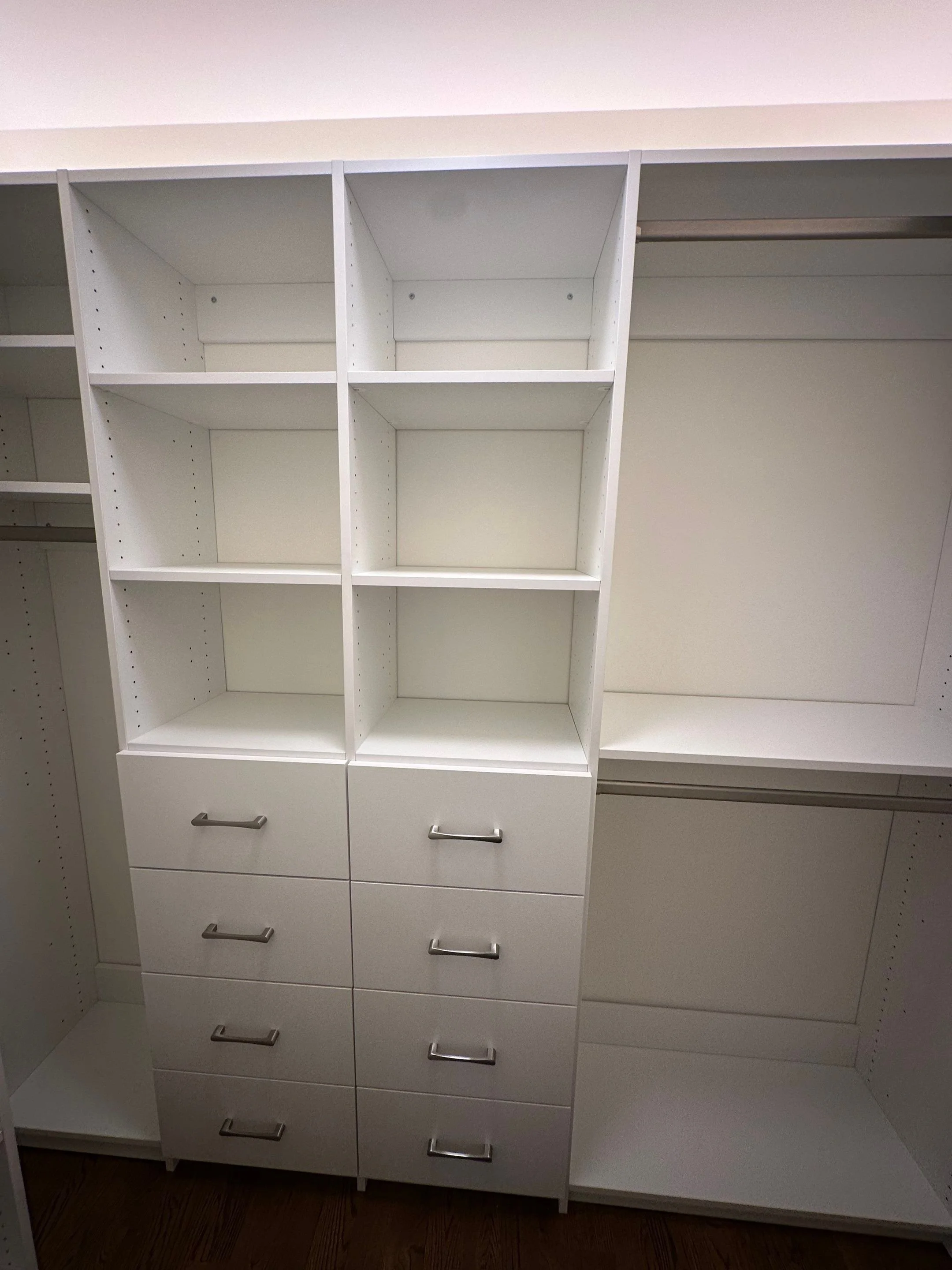 Empty white closet with shelves, drawers, and hanging spaces.