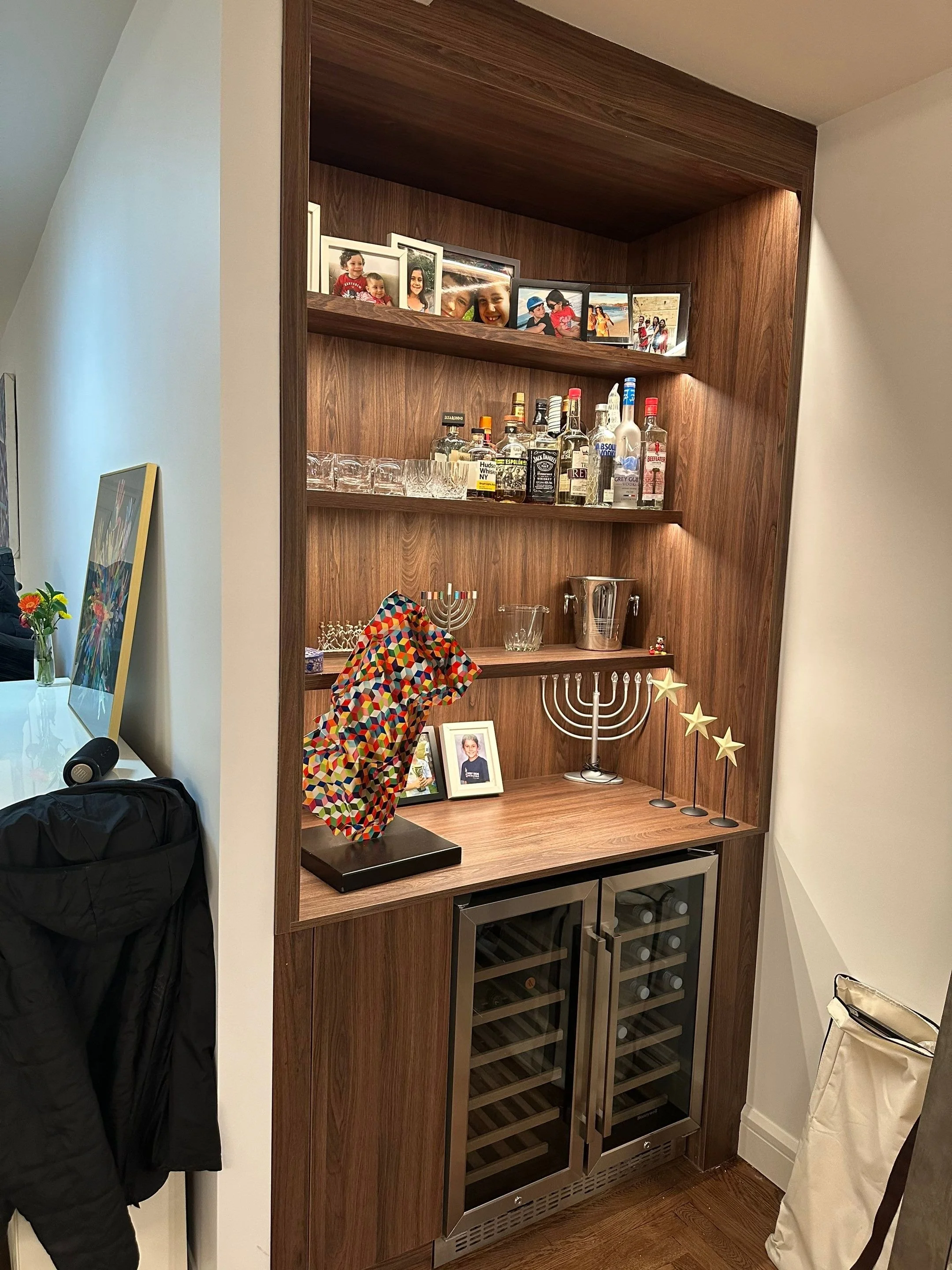 A home bar with shelves, framed photos, and holiday decorations, including a menorah and stars, in a wooden cabinet.