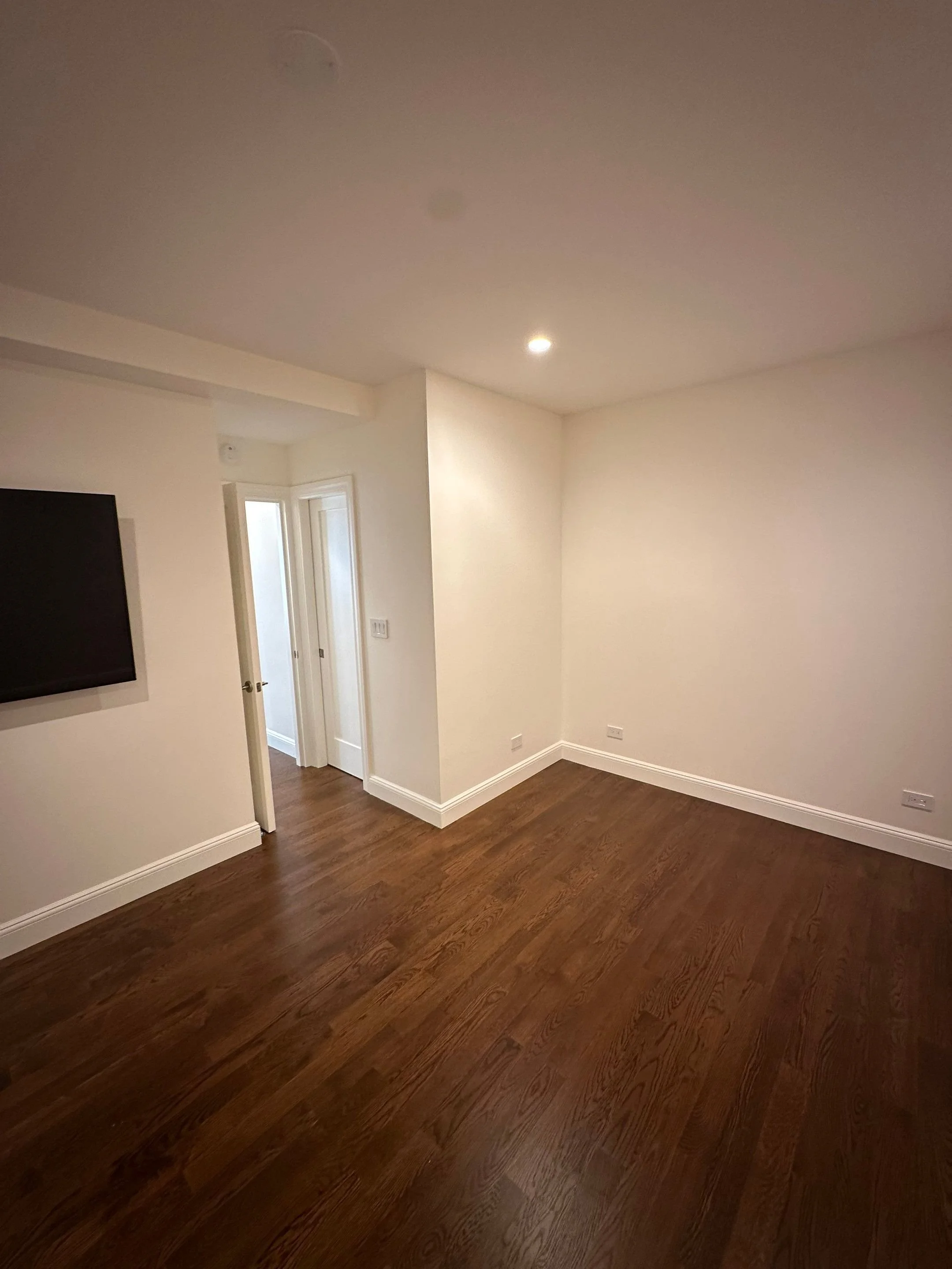 Empty room with white walls, dark hardwood floor, doorways, and a wall-mounted TV