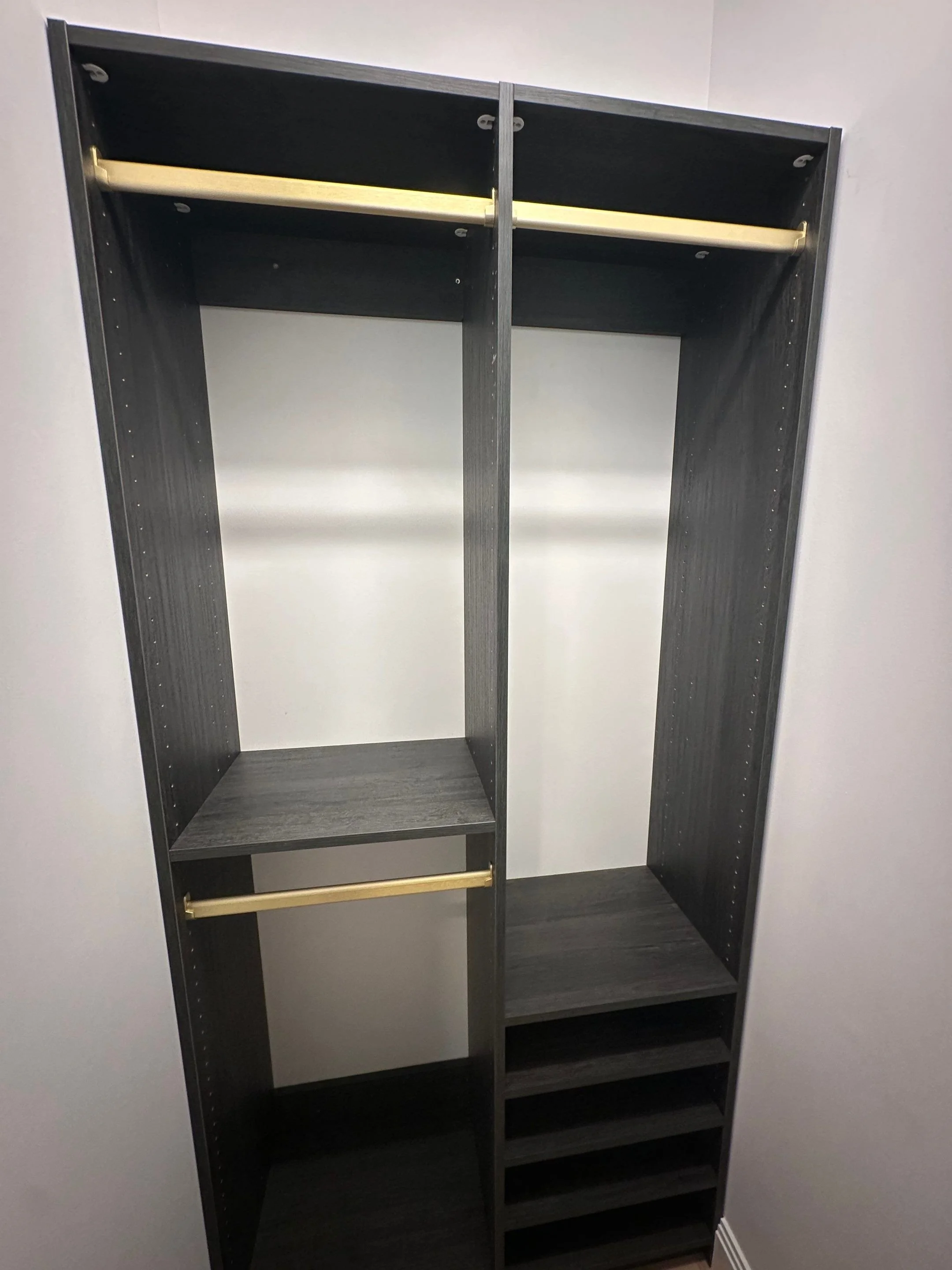 Empty black closet organizer with multiple shelves and hanging rods against a wall.