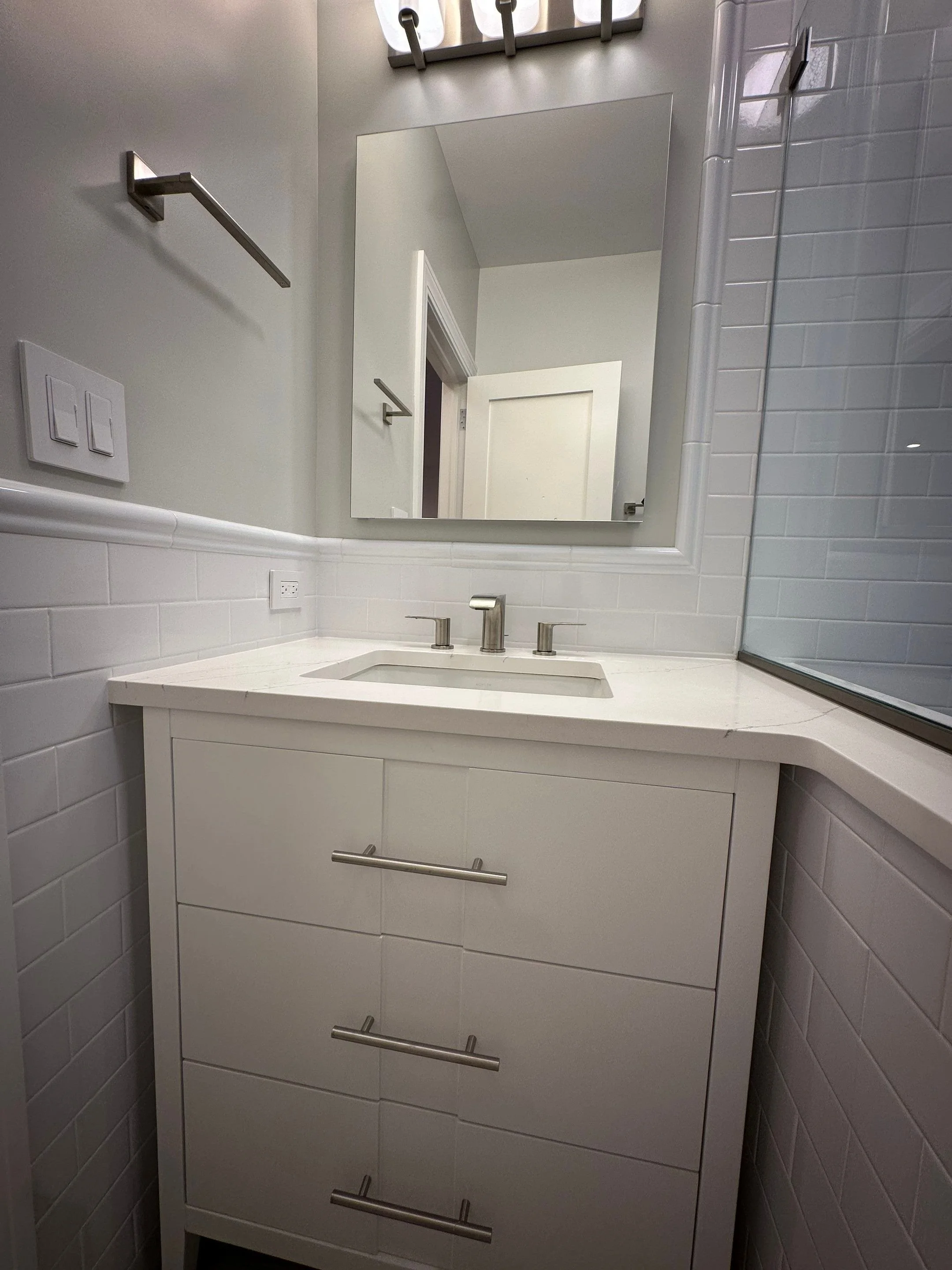 Bathroom with white vanity, faucet, mirror, and tiled wall.