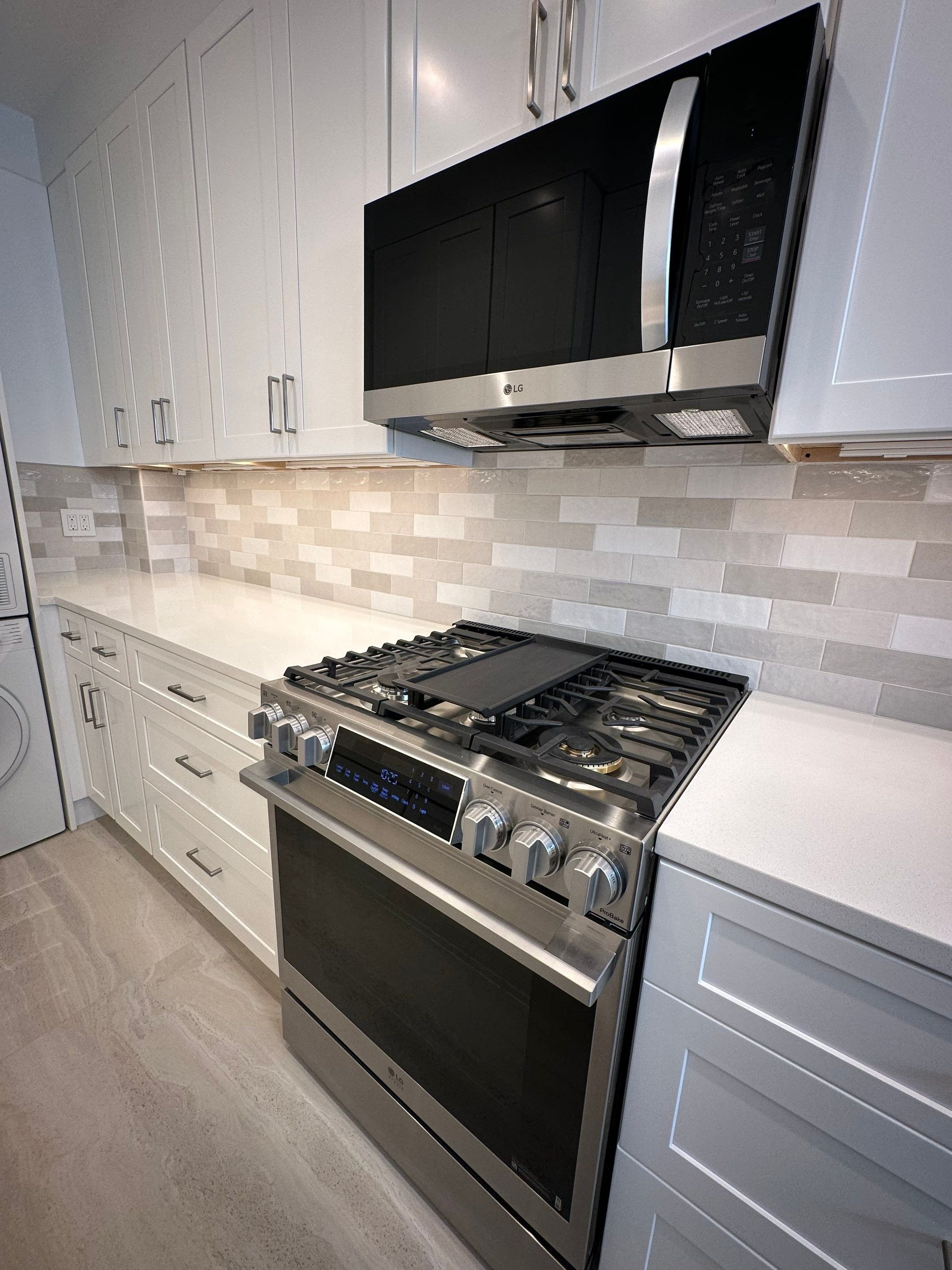 Modern kitchen featuring white cabinets, a stainless steel LG microwave mounted above a stainless steel gas stove with multiple burners, and a beige tile backsplash.