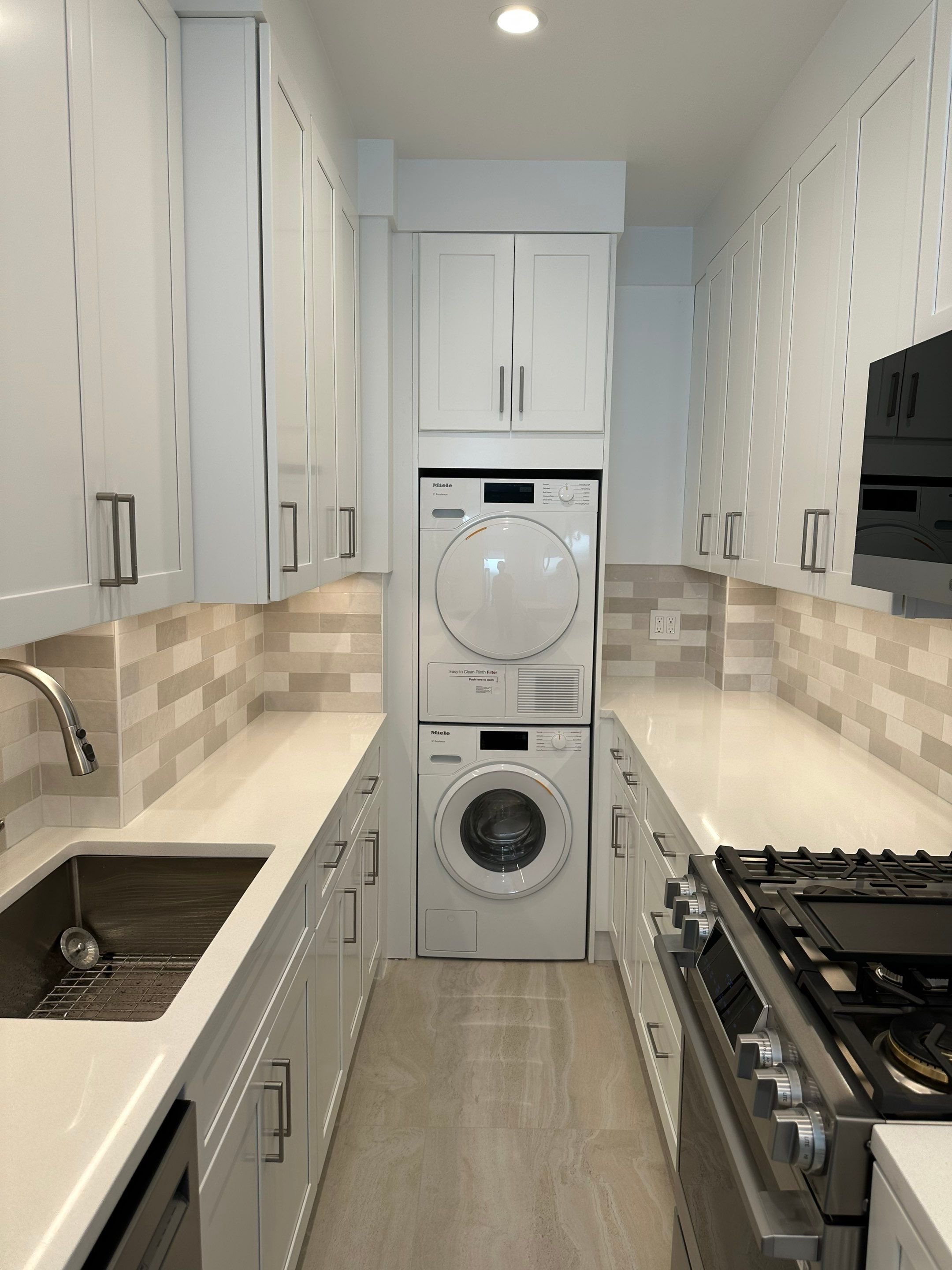 Kitchen with white cabinets, beige tile backsplash, beige floor, stainless steel stove, sink, and a stacked washer and dryer in the back wall.