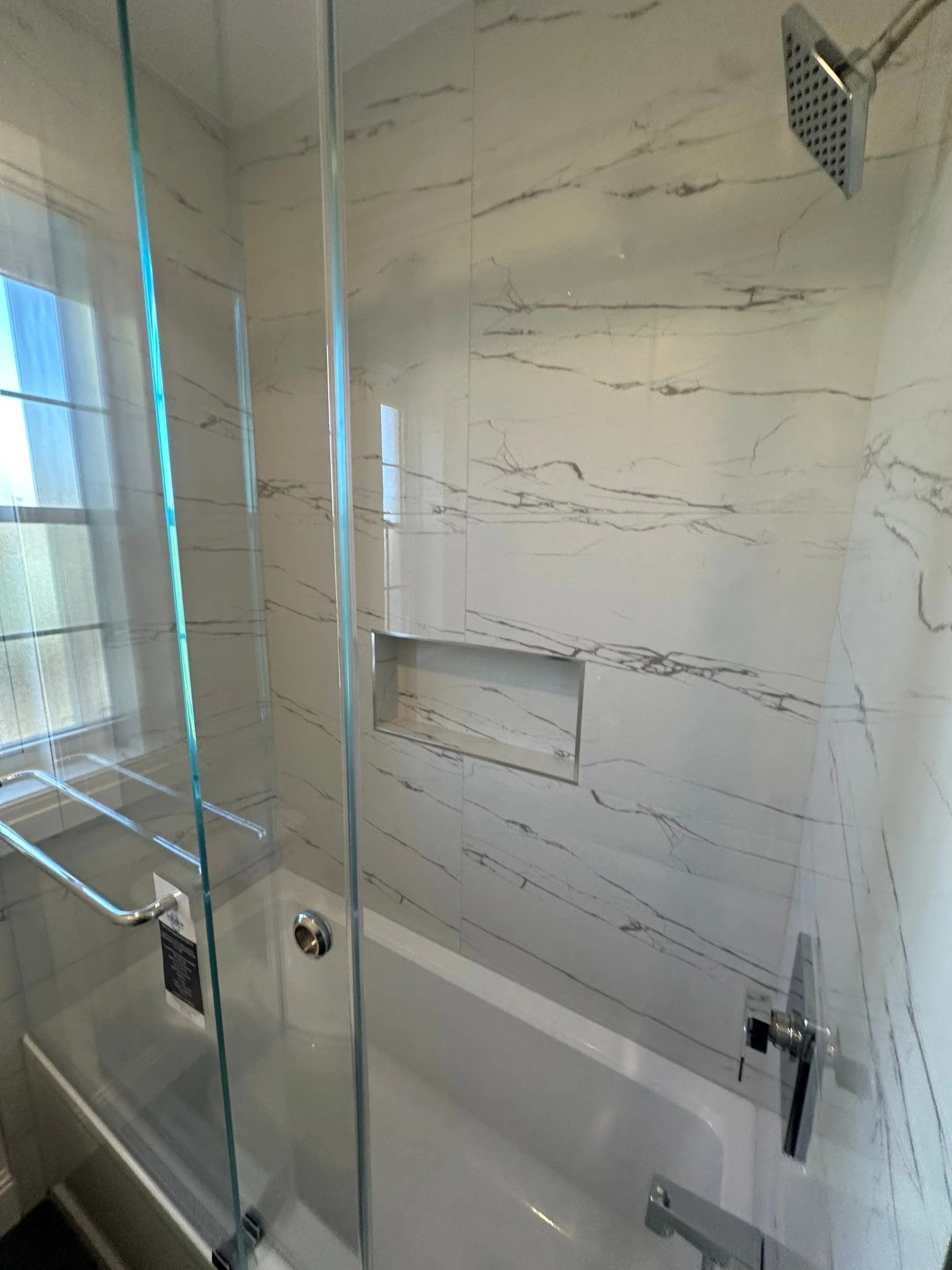 Bathroom with a bathtub, marble walls, and a glass shower door.