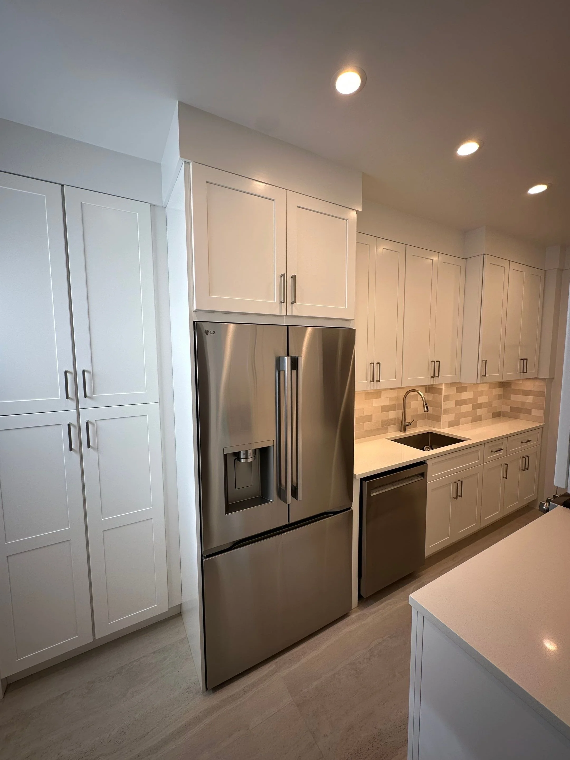 Modern kitchen with white cabinets, stainless steel LG refrigerator, dishwasher, beige backsplash, and a black kitchen sink.