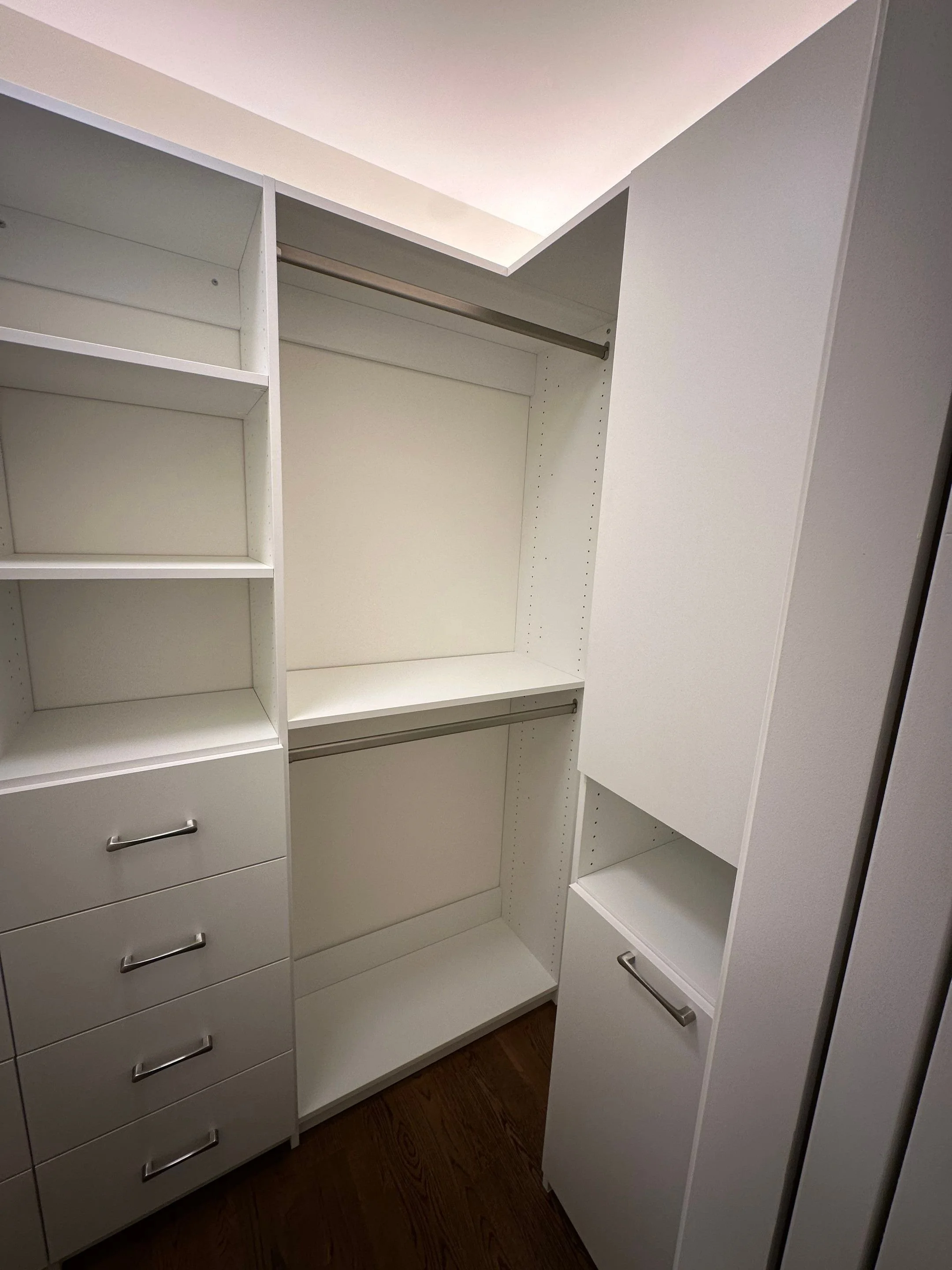 Empty white closet with shelves, drawers, and hanging rods.