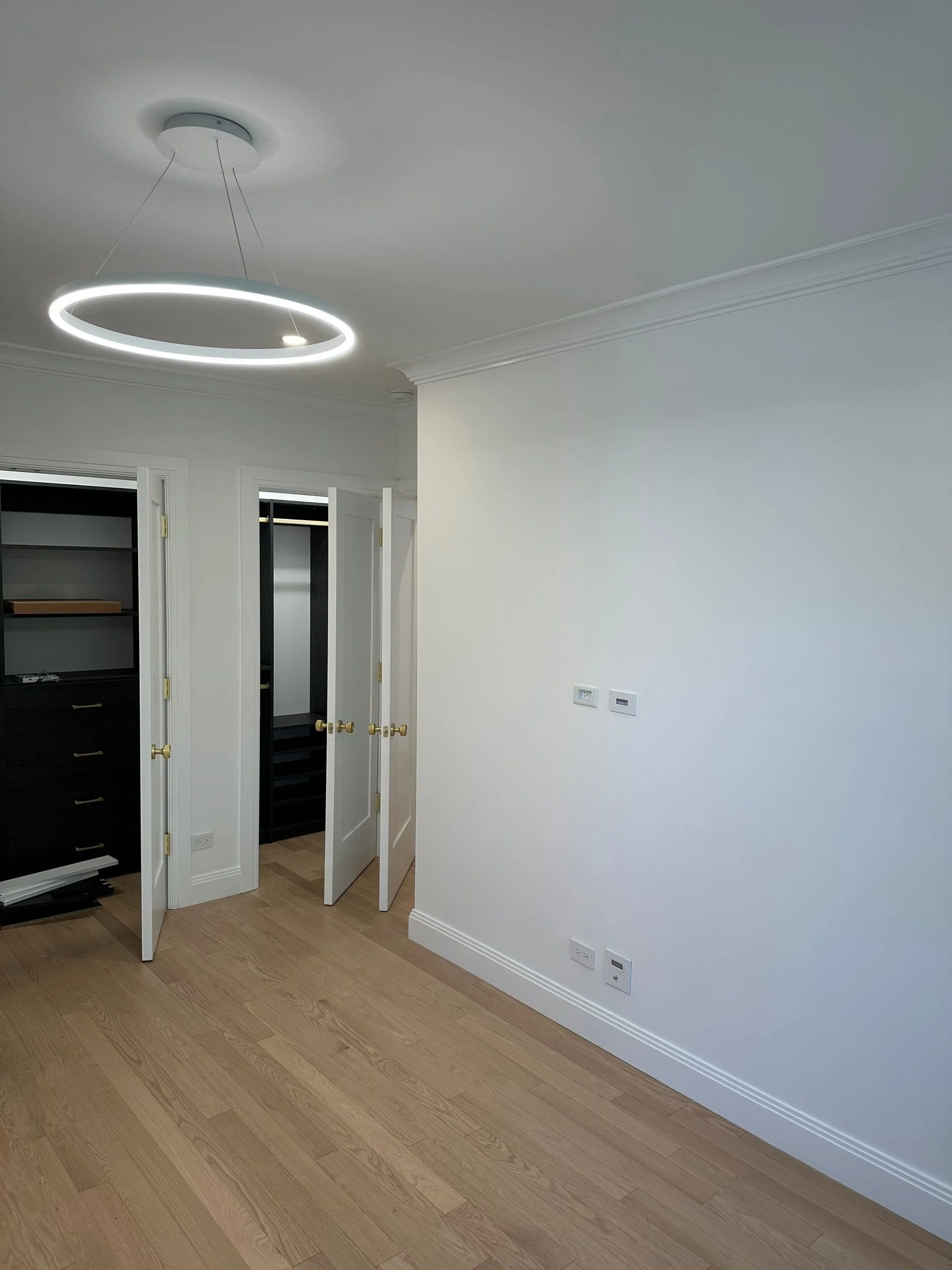 Empty room with hardwood flooring, white walls, open closet doors, and modern circular ceiling light fixture.
