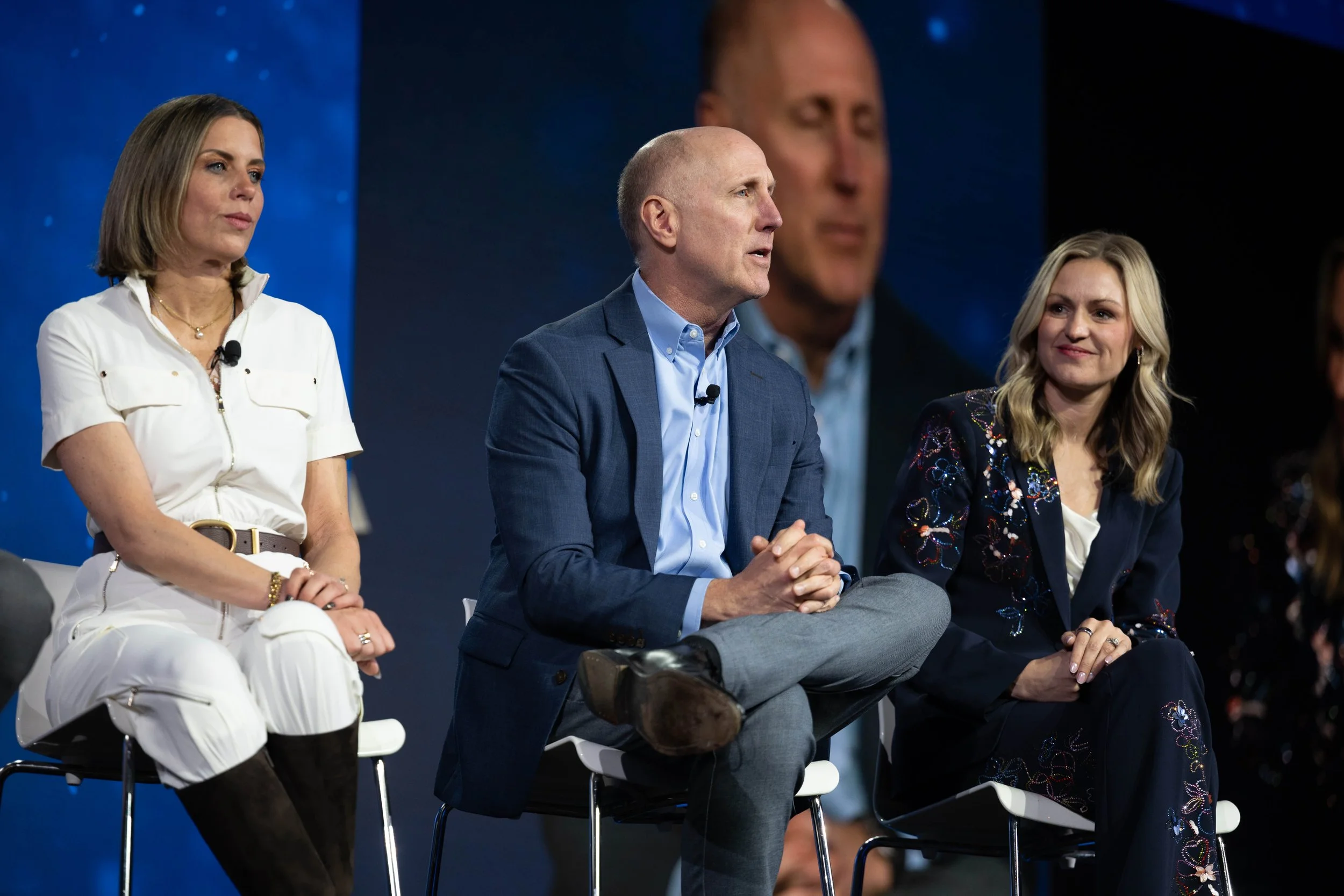 A man sits with other panel speakers on stage - conference photography