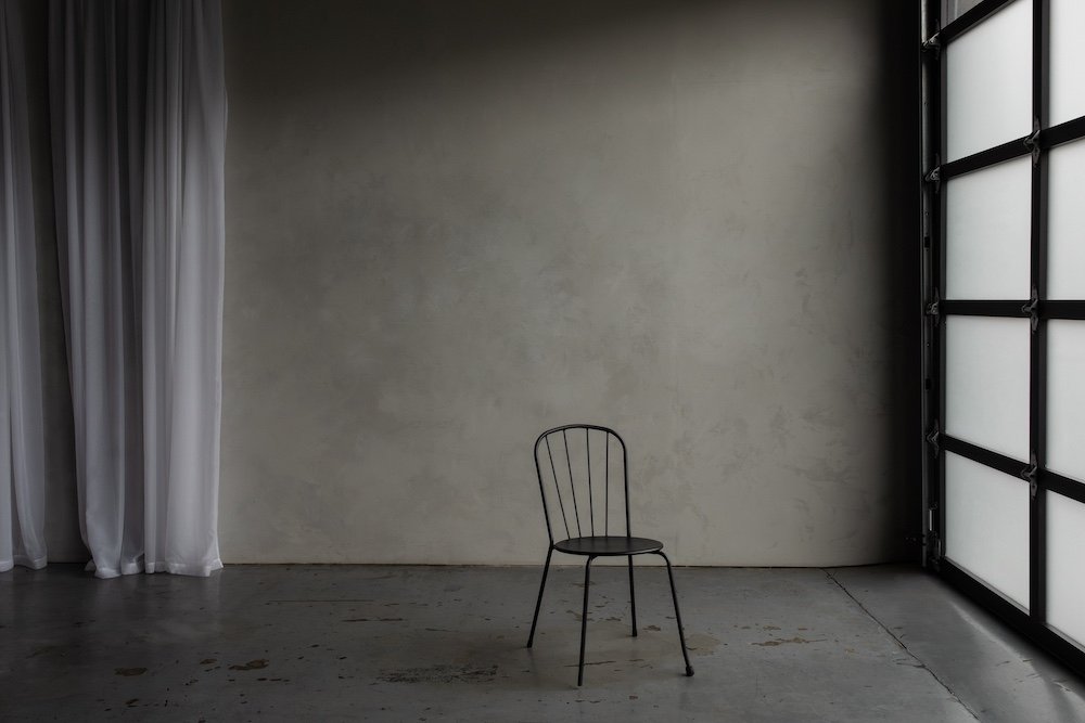 A simple photo studio with texture gray walls, gray concrete floor and single black cafe chair