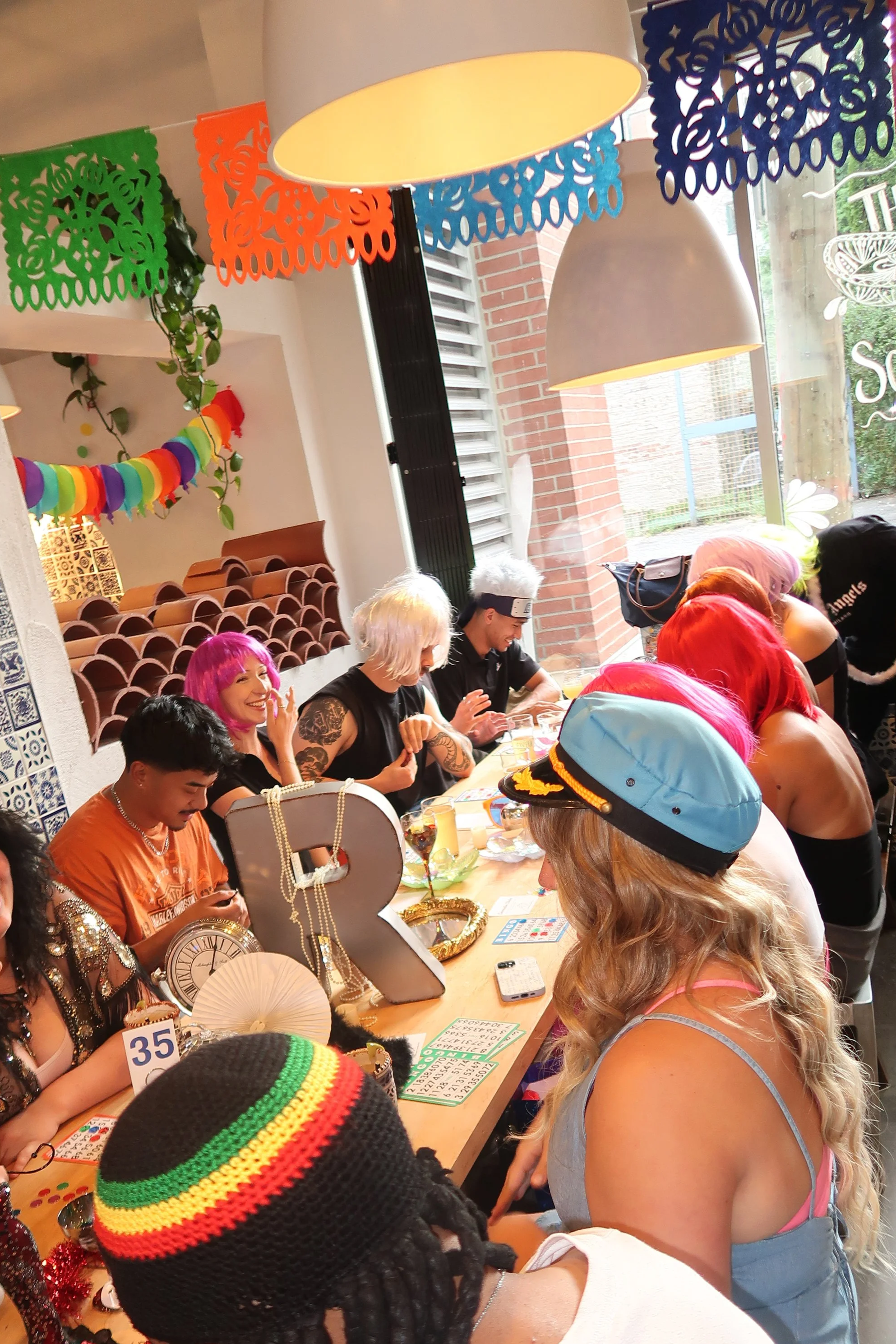 Group of people with colorful hair and costumes sitting around a table decorated for a celebration or party.