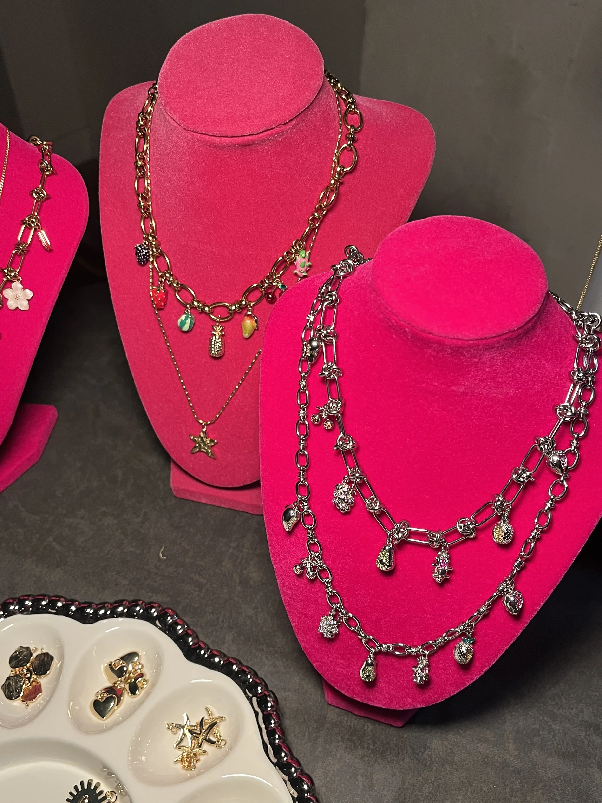 Display of various necklaces on pink velvet busts and earrings on a white jewelry tray.