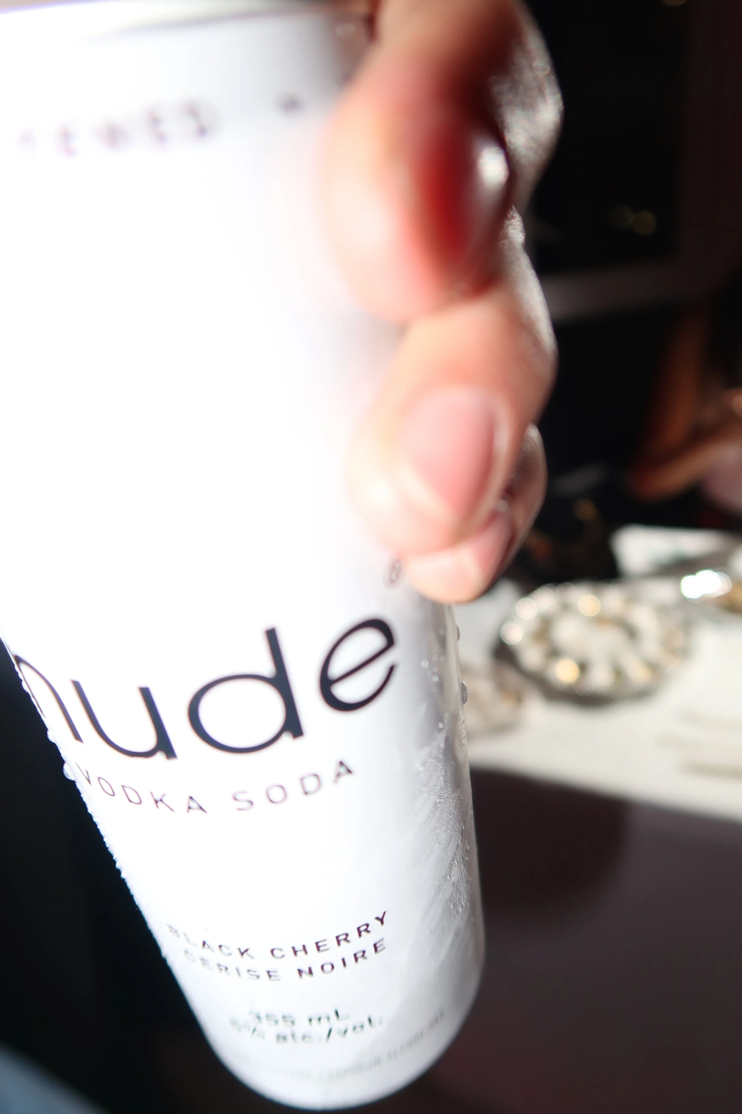 Close-up of a person's hand holding a white can of Sparkling Ice water flavored with black cherry and cherry noir, with a blurred background.