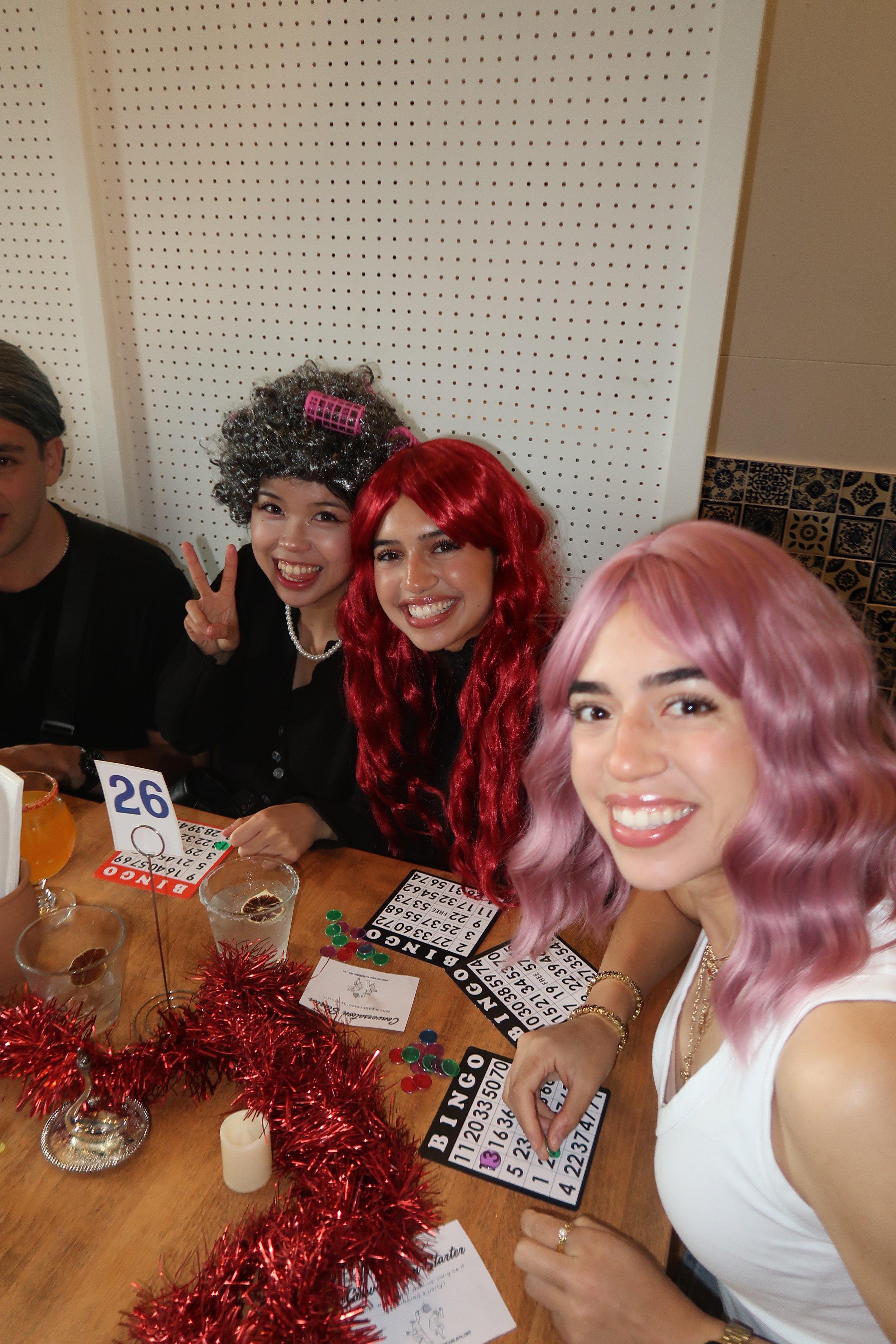 Group of people celebrating New Year's Eve with bingo, colorful decorations, and drinks at a table.