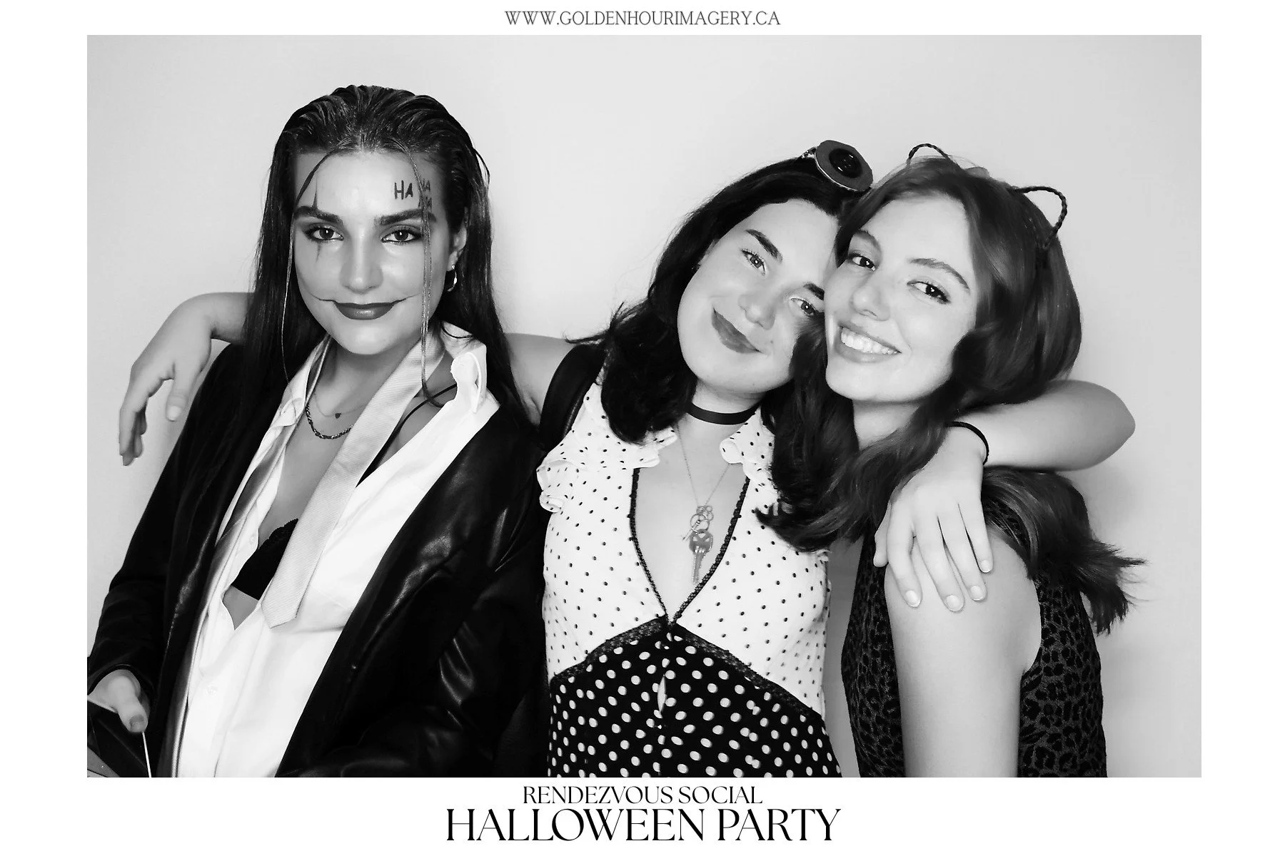 Three women smiling and embracing at a Halloween party, dressed in costumes with makeup, accessories, and themed outfits, black-and-white photograph.