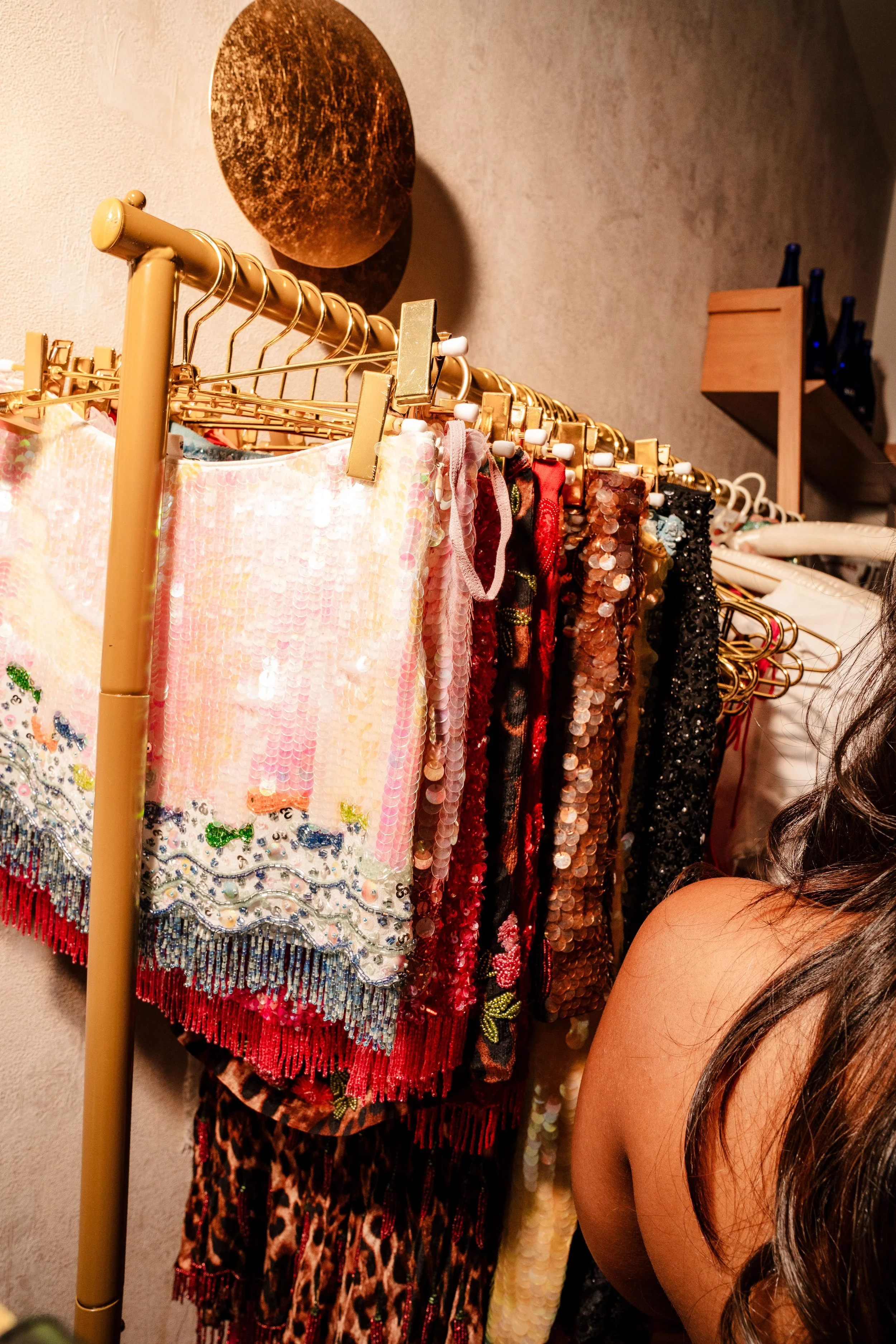 Colorful and sequined dresses hanging on a gold clothing rack.