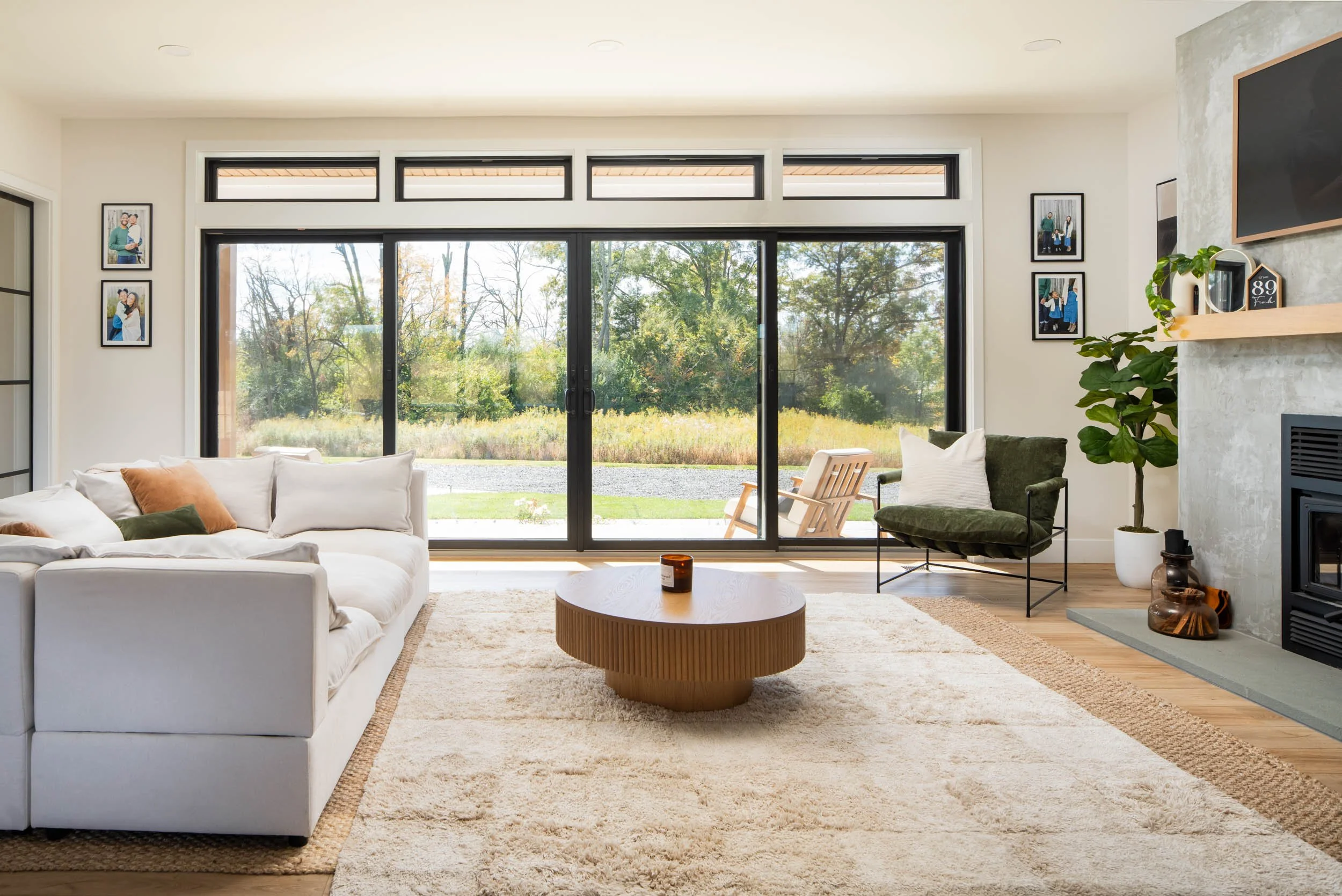Bright living room with white sofa, green armchair, and sliding glass doors overlooking a yard with trees.