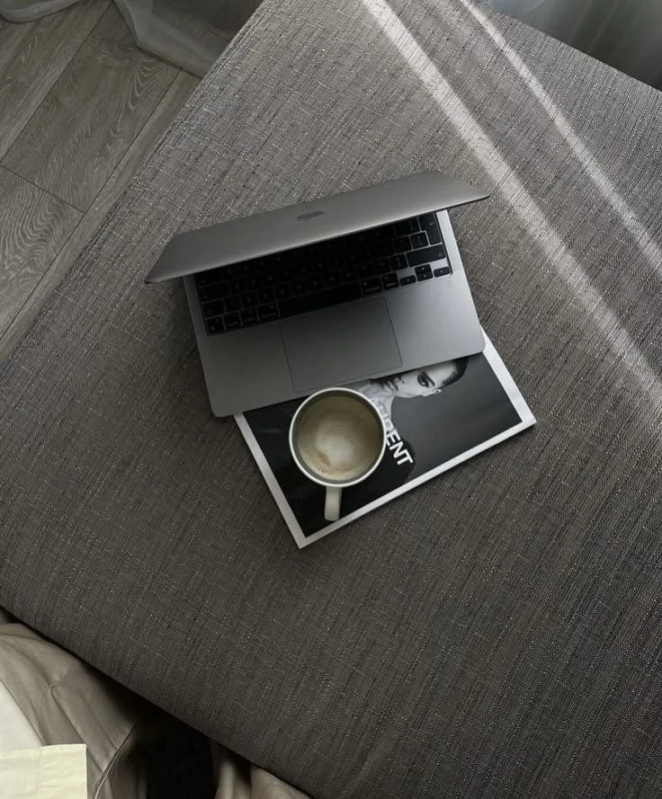 An open laptop resting on a magazine with a coffee cup sitting on top of the magazine.