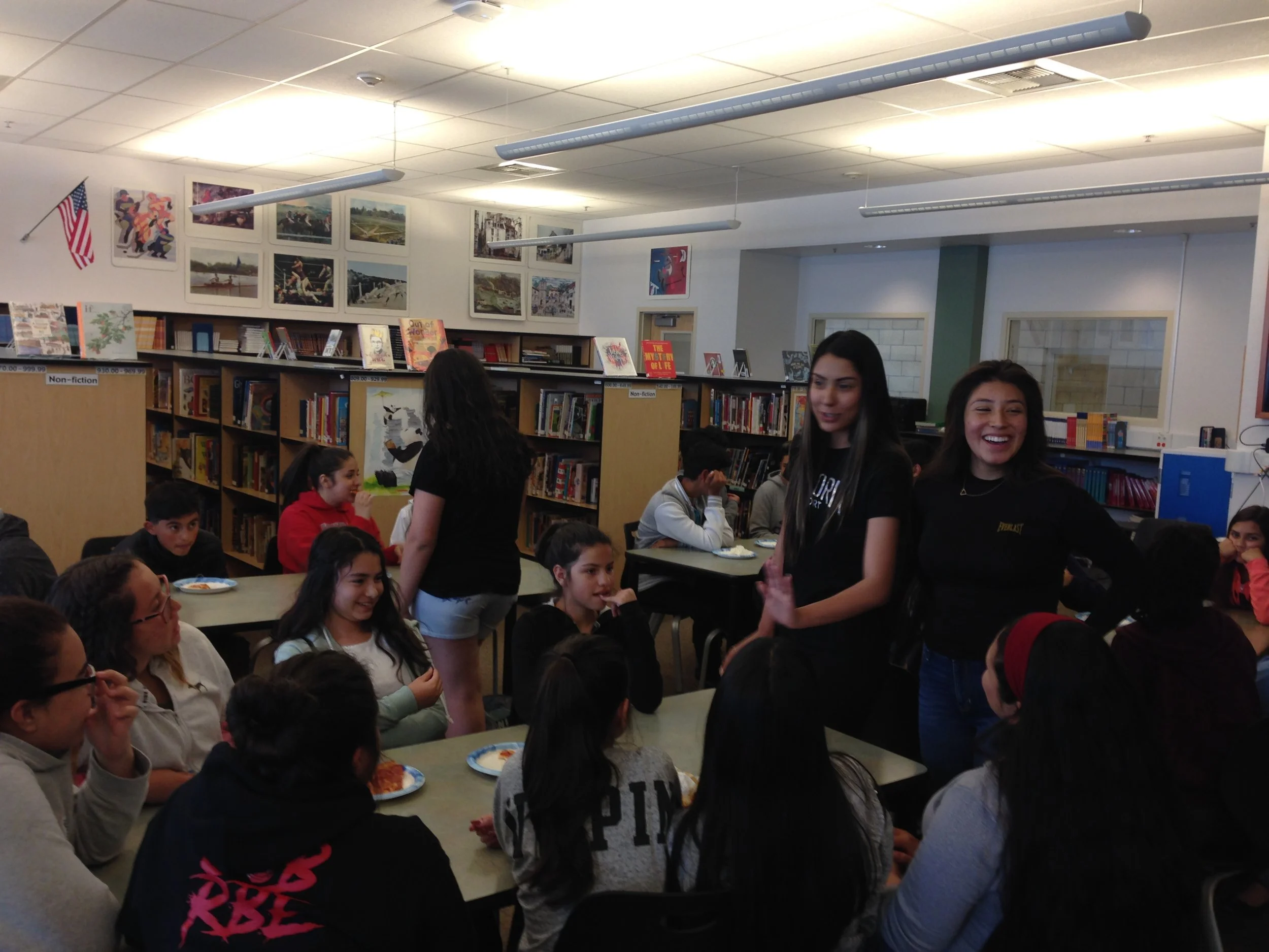 Students and teachers gathered in a school library, engaging in conversation and smiling.