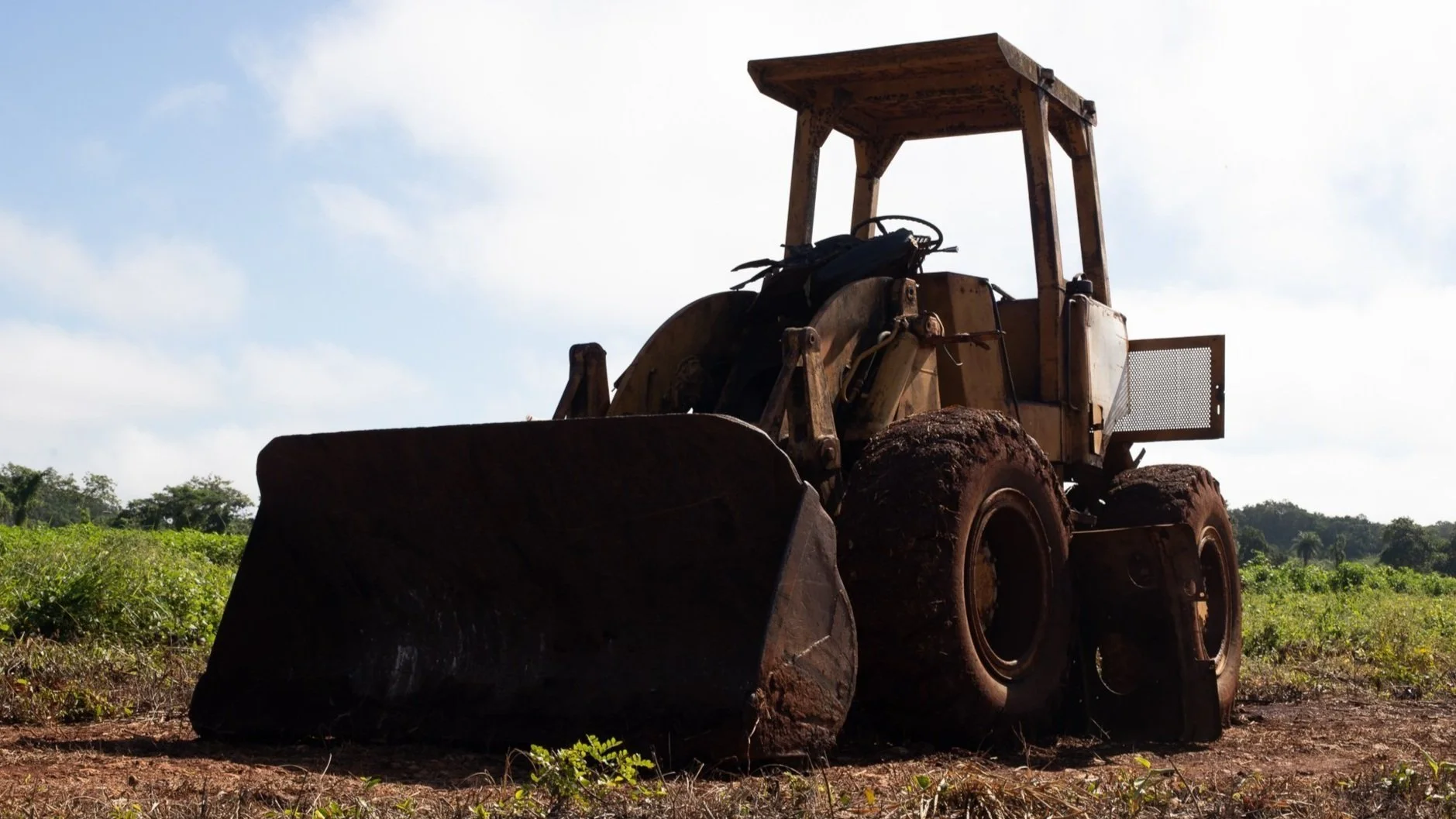 Excavadora vieja en un campo de tierra y vegetación, con cielo nublado.