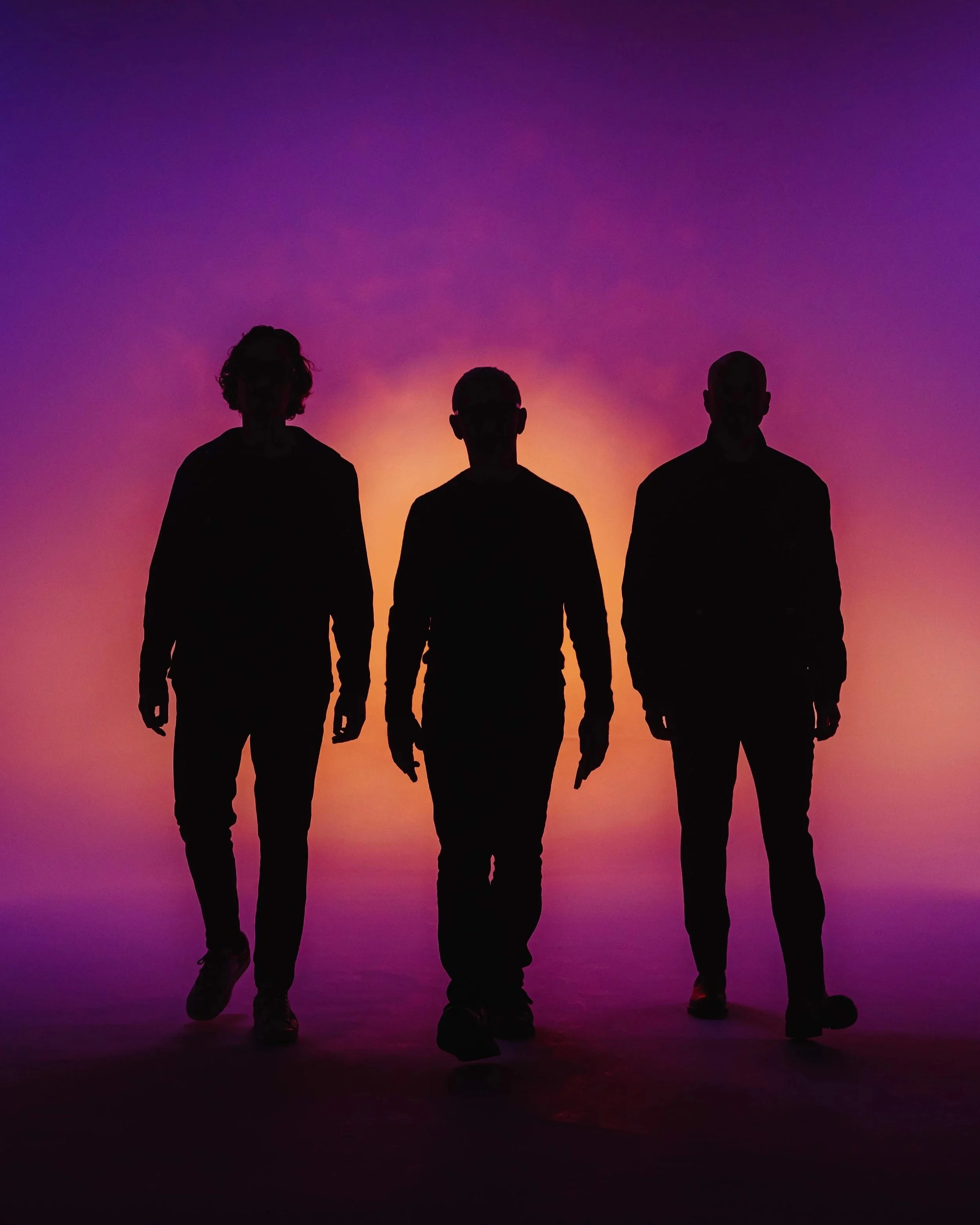 Above and Beyond. Silhouettes of three people walking on a stage with a colorful sunset background.