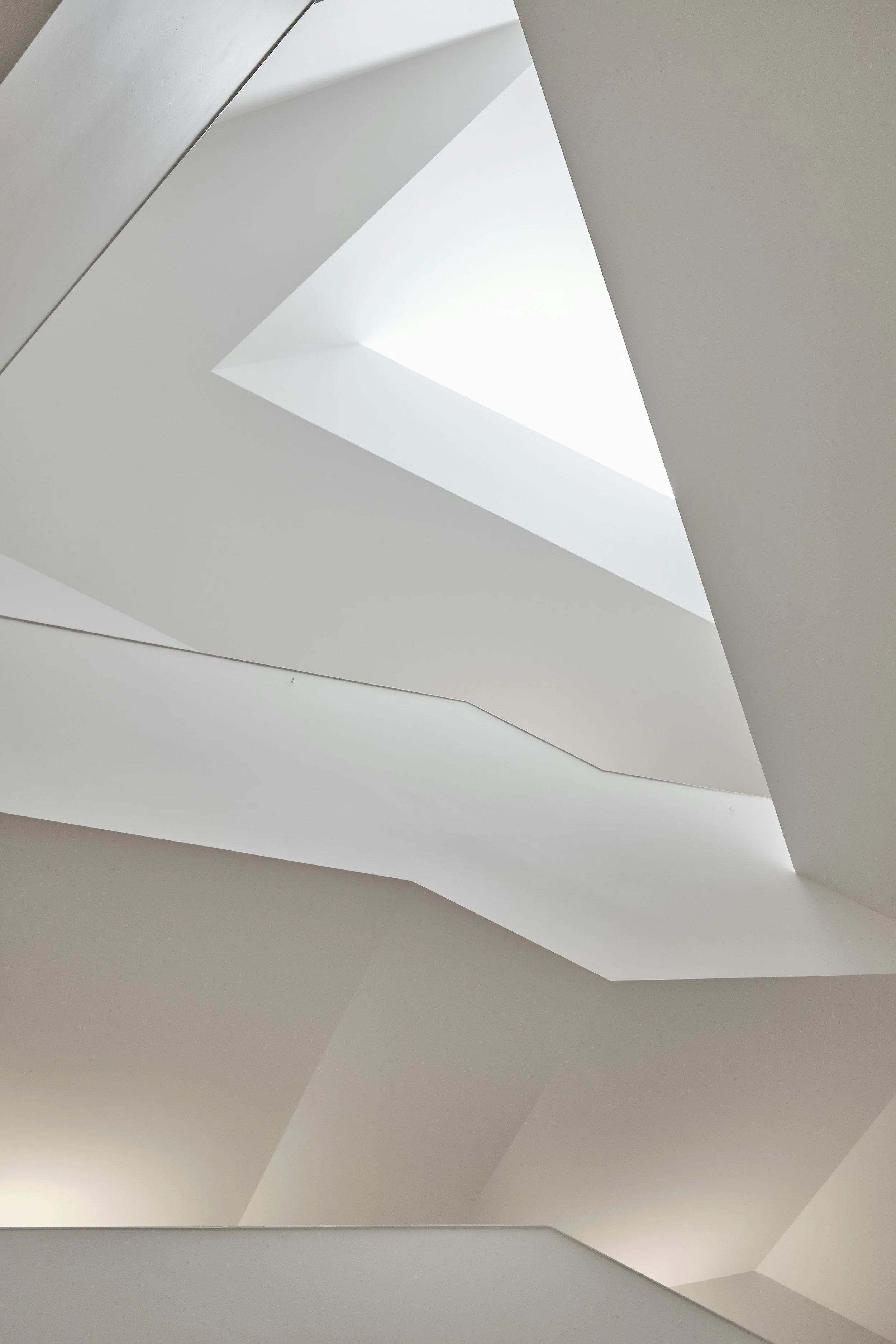 Interior view with geometric white architectural design and natural light coming through a triangular skylight.