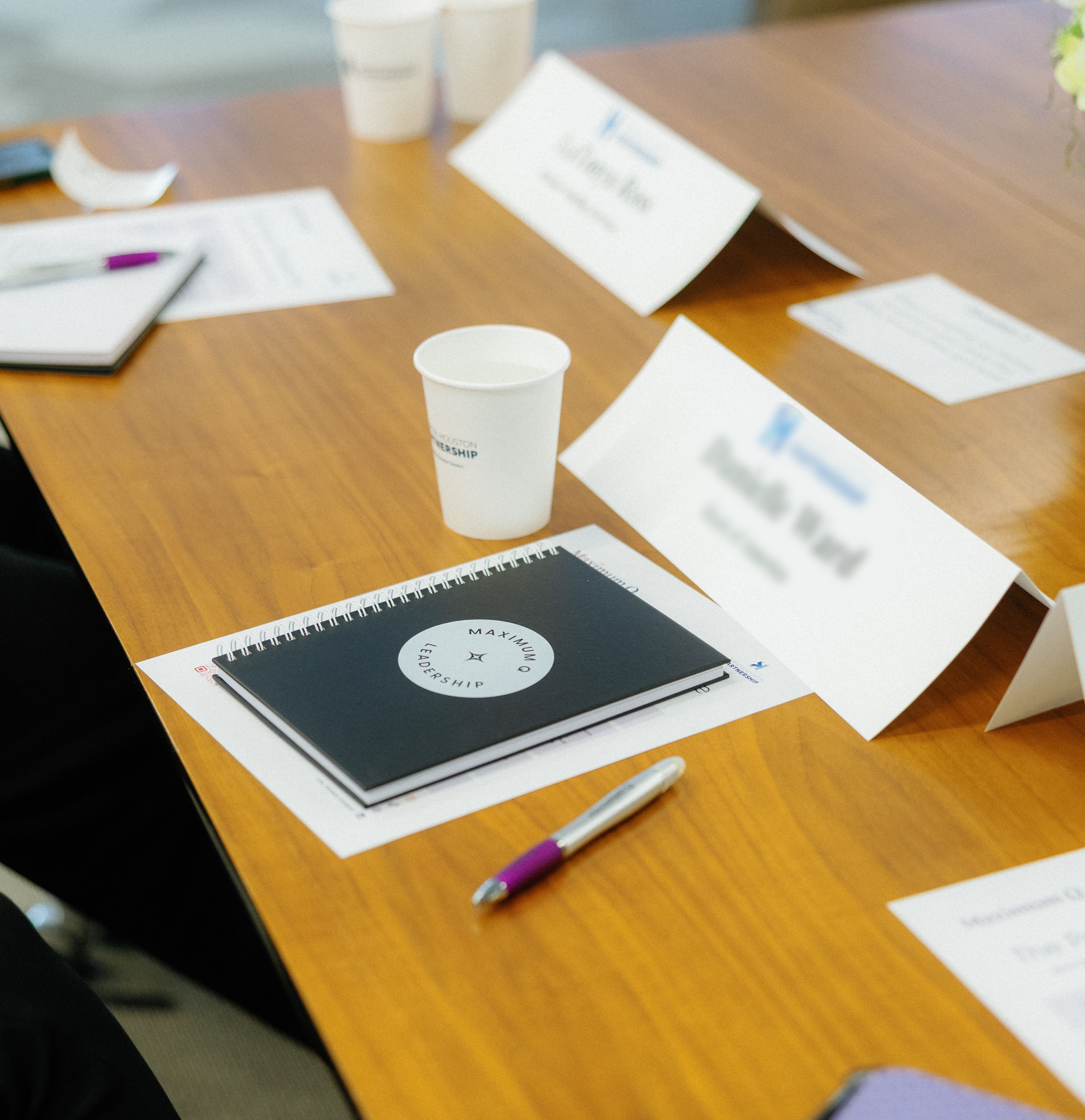 Blurred view of a discussion table with papers, pens, and cups, indicating a meeting or workshop setting.