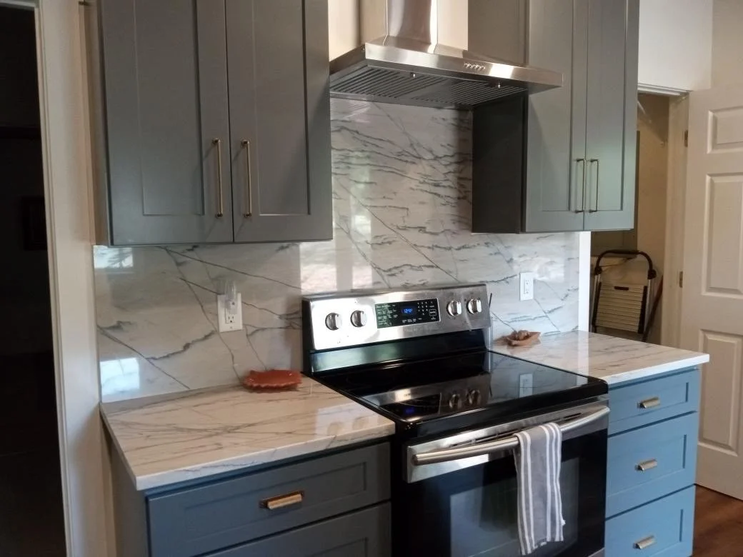 Kitchen with gray cabinets, marble backsplash, and black stove with oven, with a striped towel hanging on the oven handle.