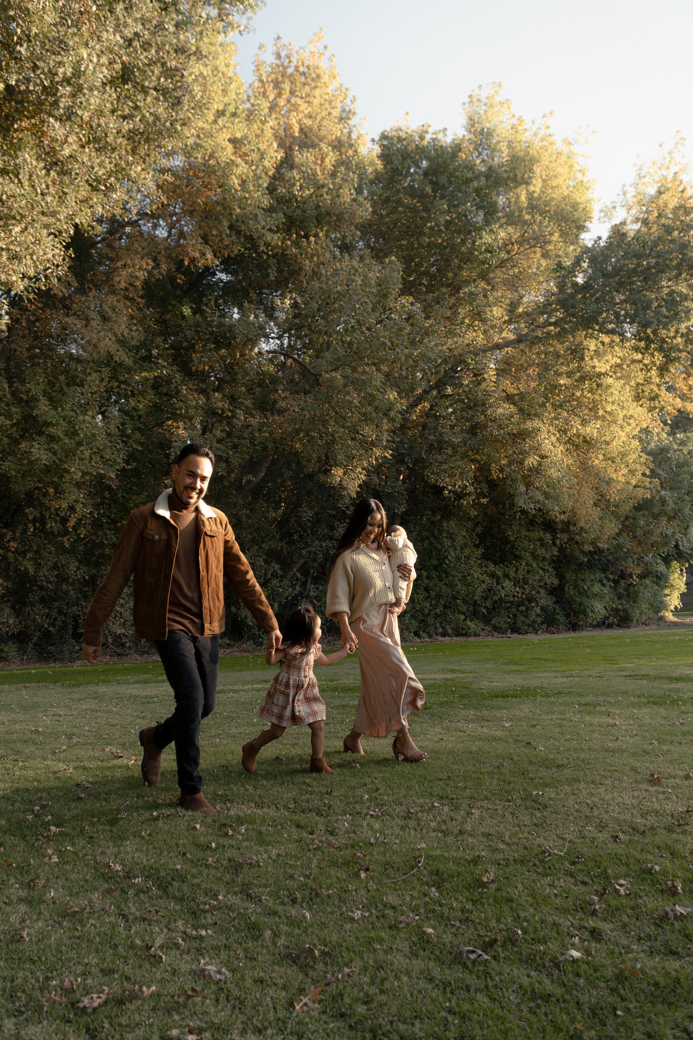 Family walking and holding hands in a park with trees and grass at a park in Modesto, California.