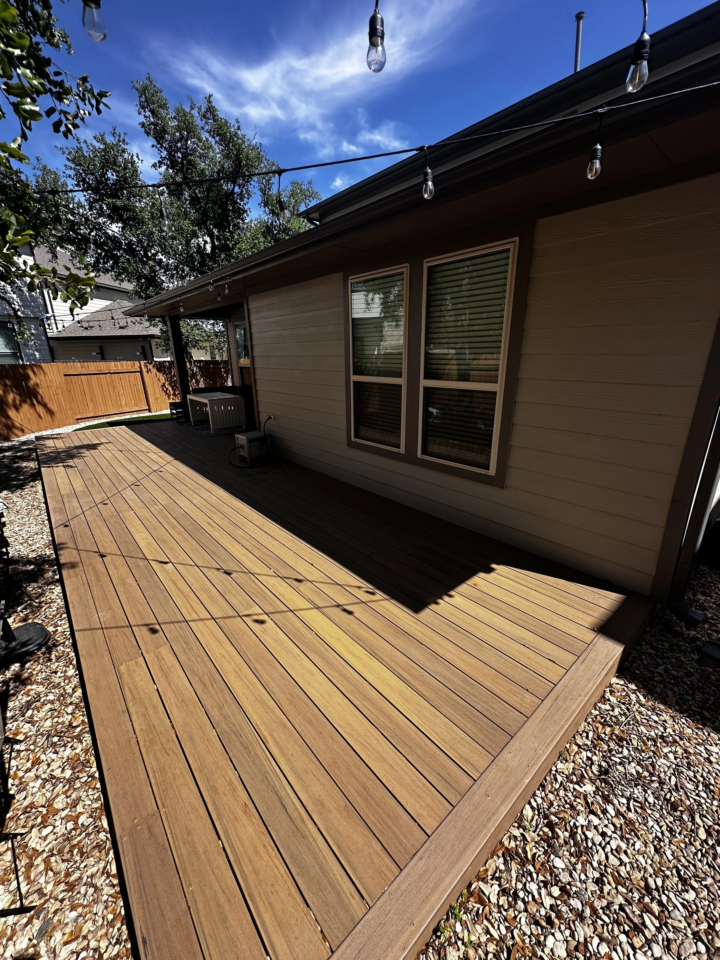 Custom wood deck installation by Golden View Landscape Design featuring modern horizontal planks, overhead string lighting, and a pea gravel landscape border in a residential Austin backyard.