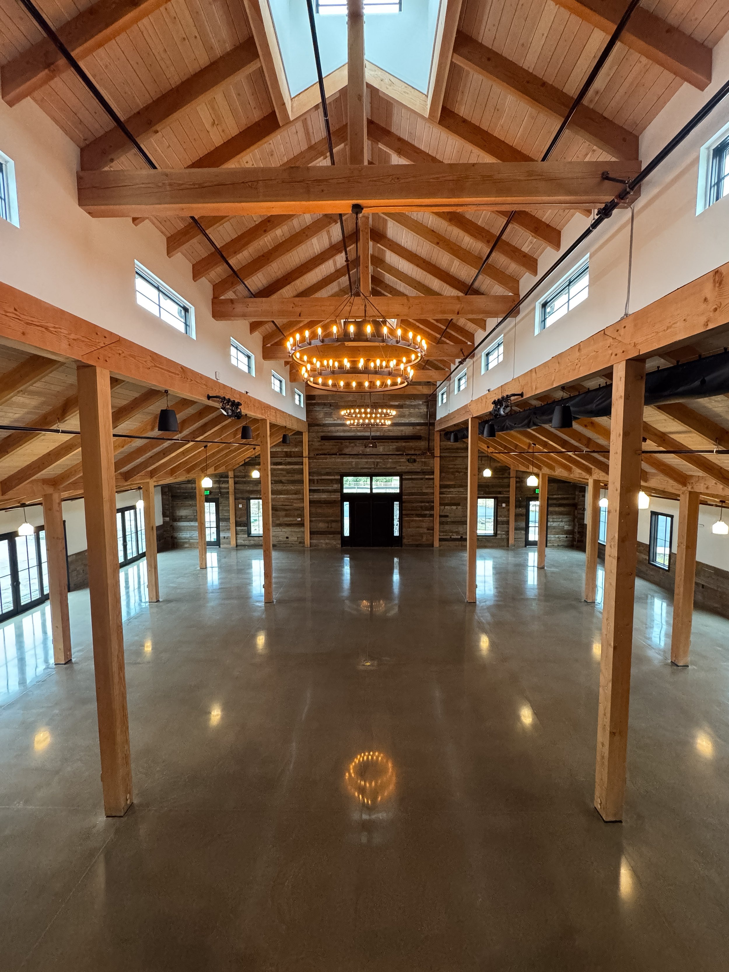 Interior view of a building under construction with wooden beams, high ceilings, and multiple windows; construction equipment and materials are scattered on the floor.