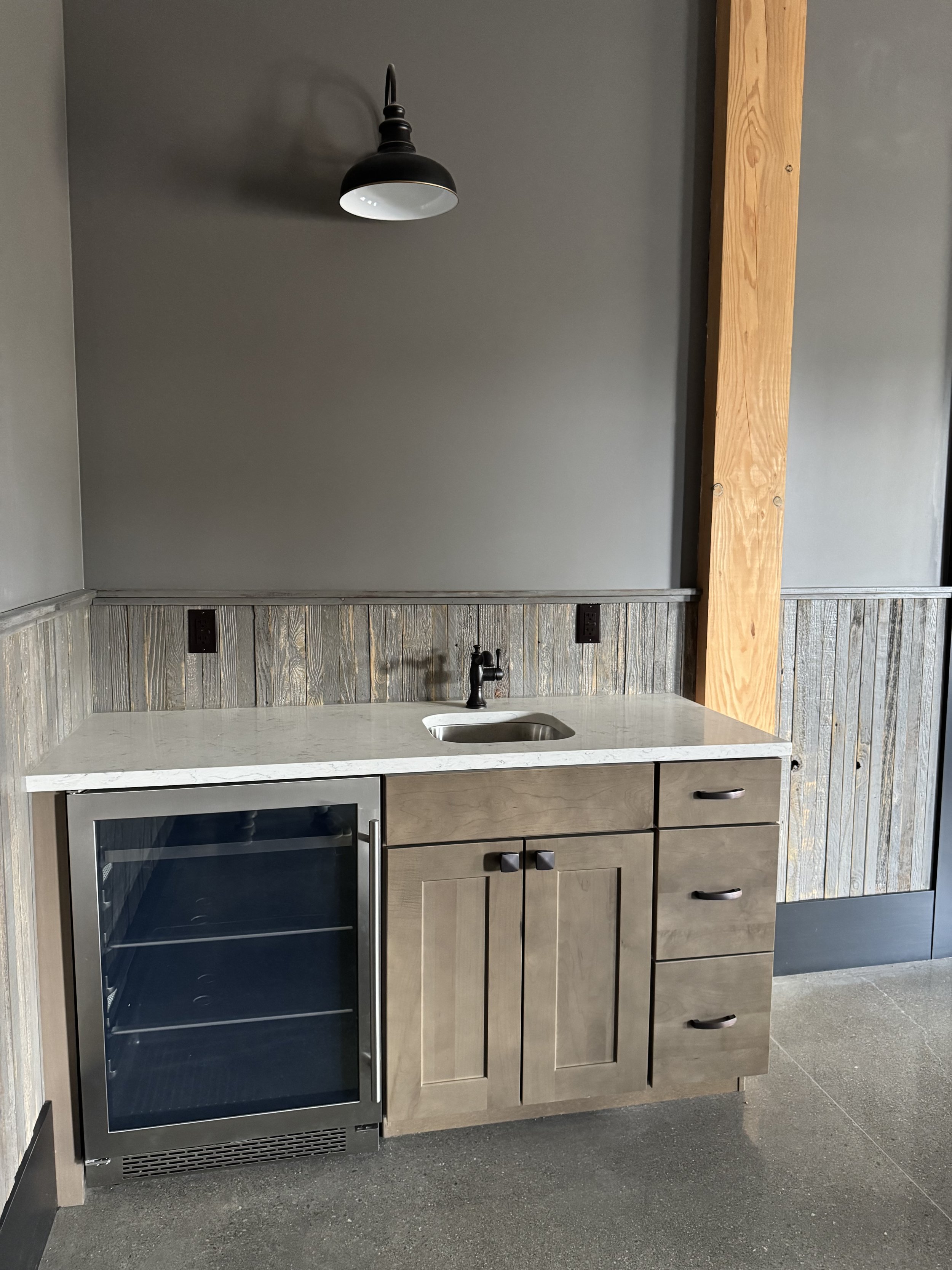 small bar with a sink, mini fridge, cabinets and black farmhouse light above