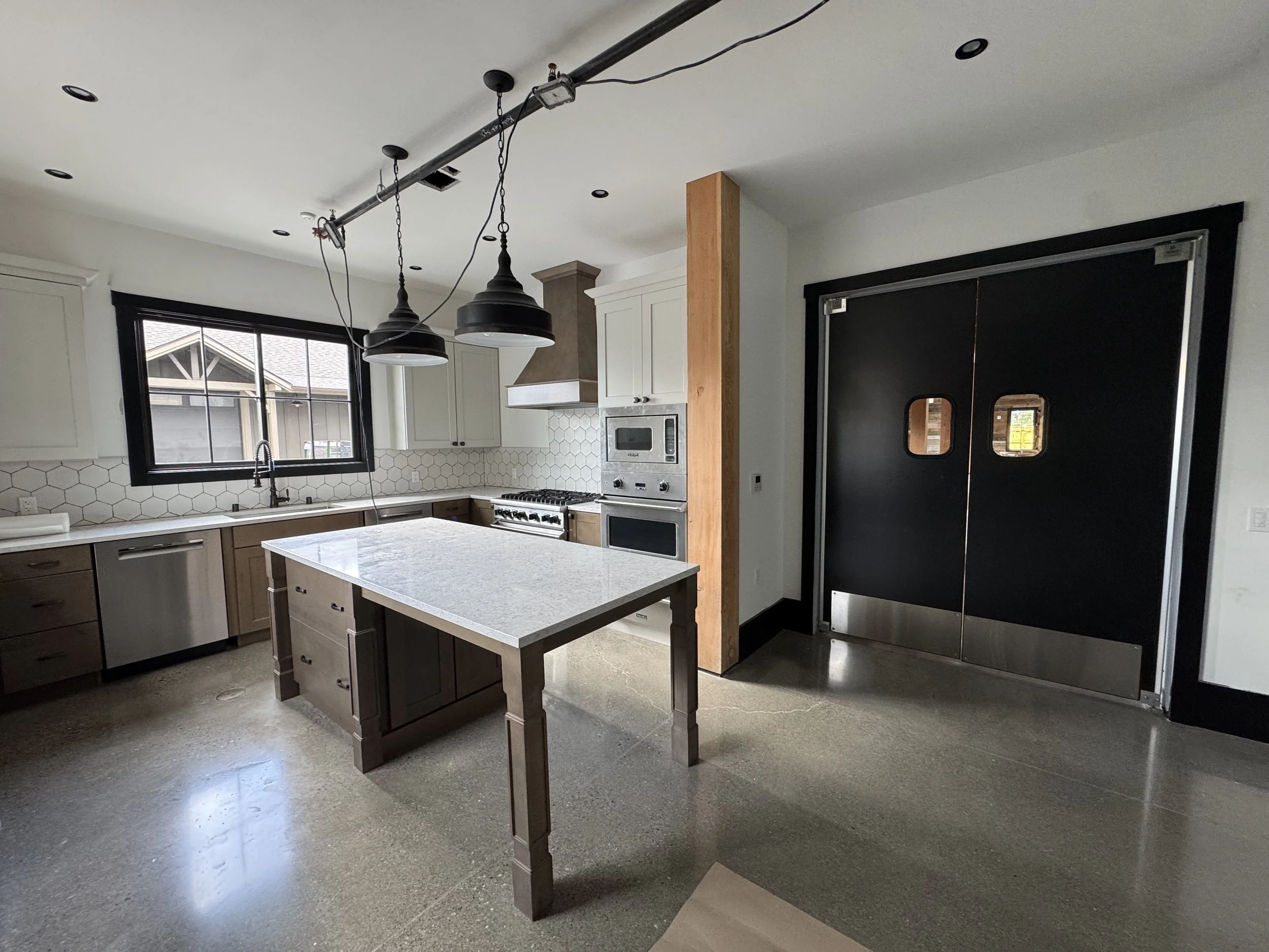 Kitchen with white walls, two windows, exposed wiring, and wooden support beams.